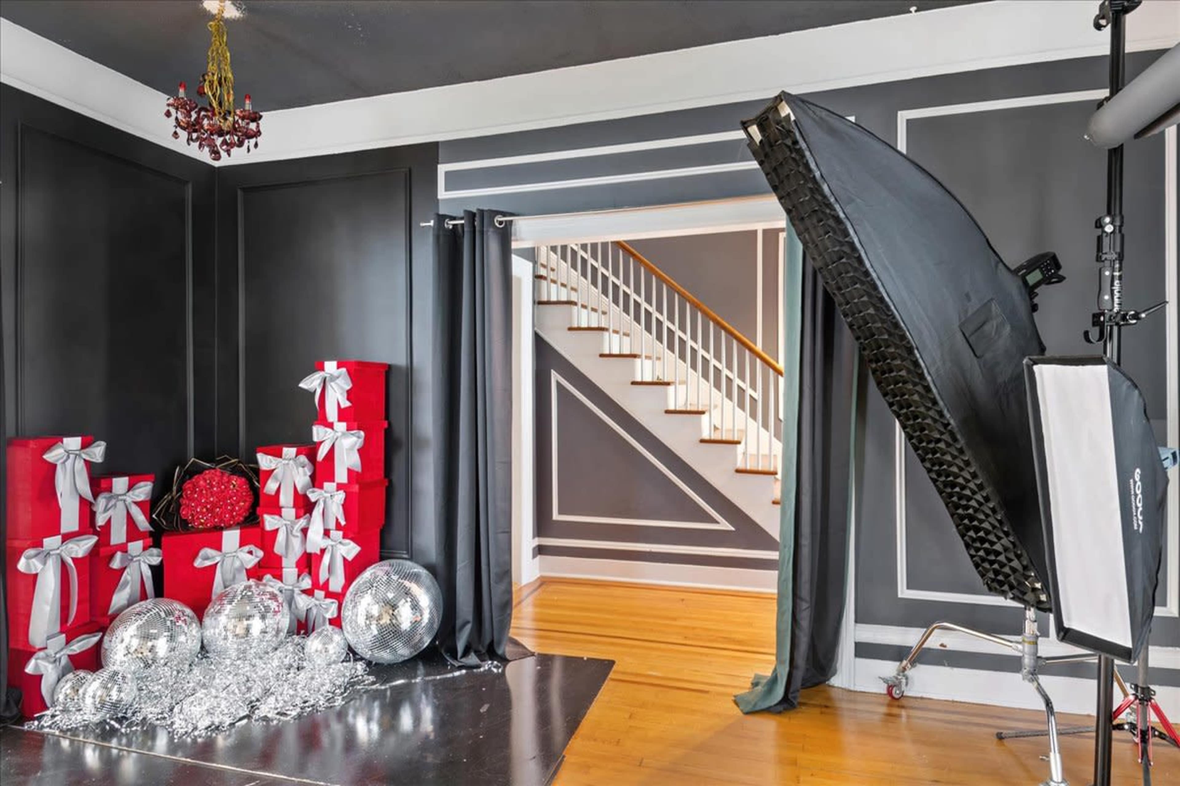 The image shows a modern interior space featuring a staircase, black walls, and a decorative setup with red gift boxes, silver balloons, and a light fixture.