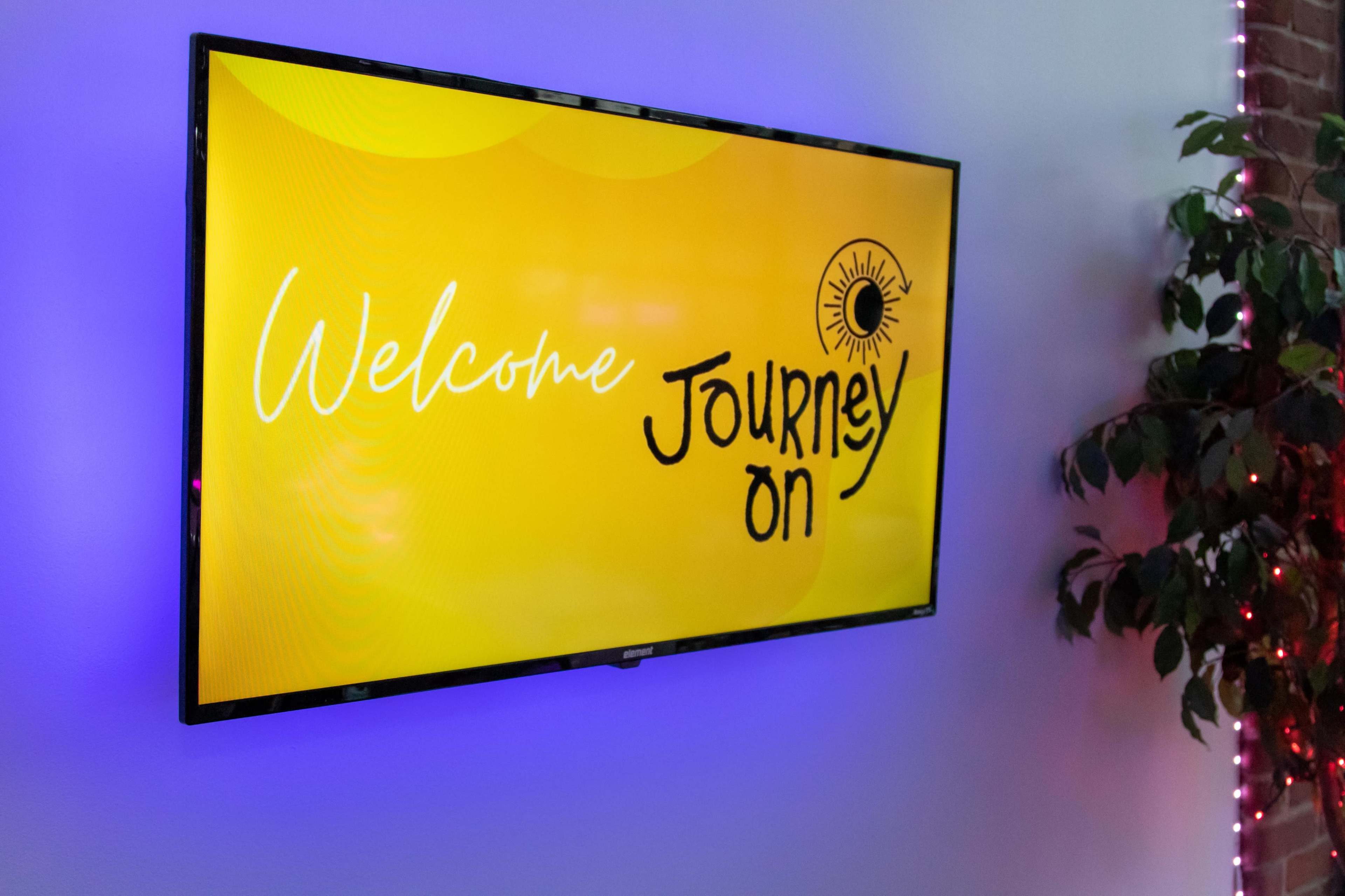 A wall-mounted screen displays a colorful welcome message that reads, "Welcome Journey On."