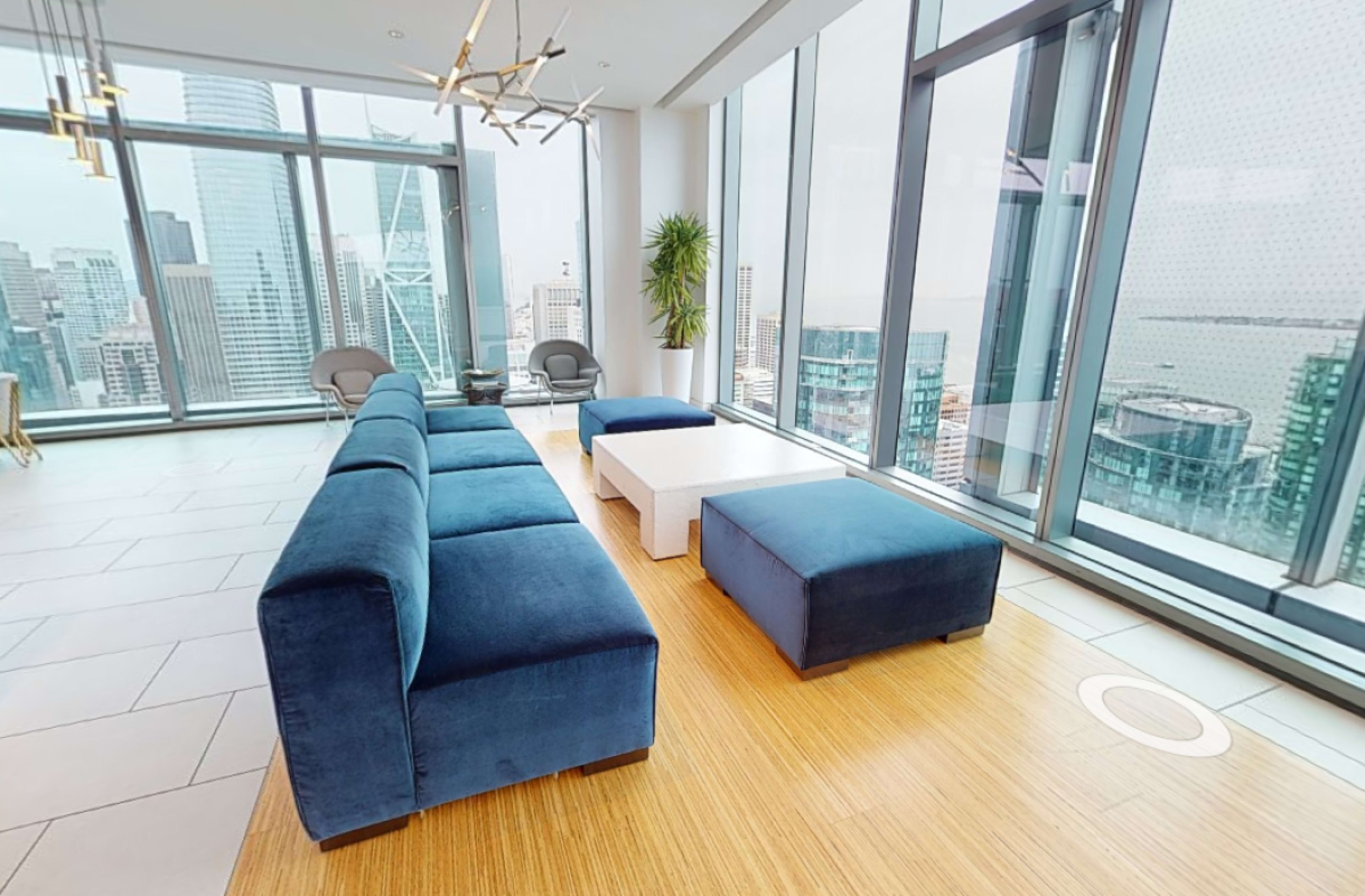 A modern lounge area features a blue sectional sofa, a white coffee table, and large windows overlooking a city skyline.
