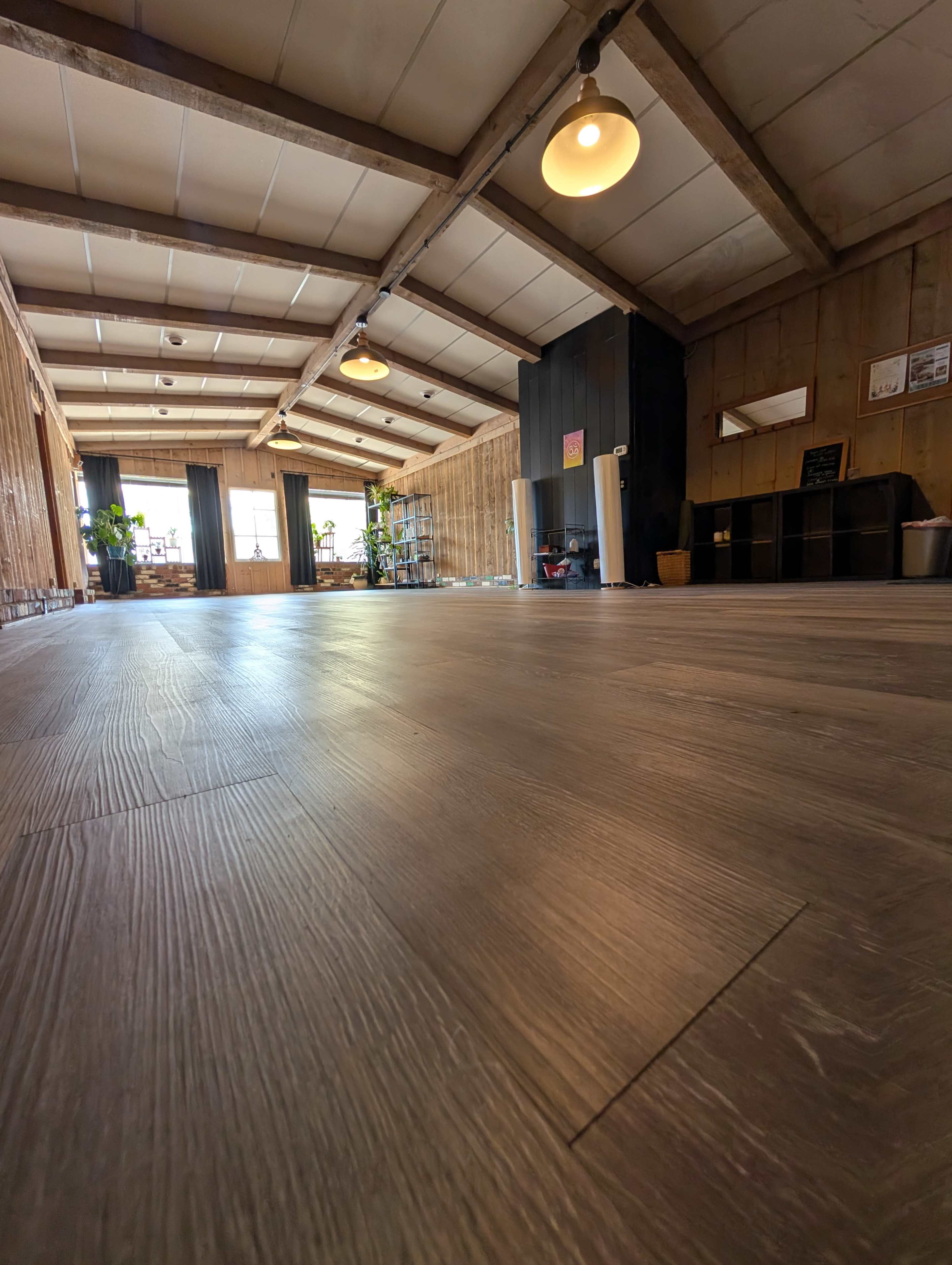 The image shows a spacious interior with wooden flooring, large windows, and minimalist decor.