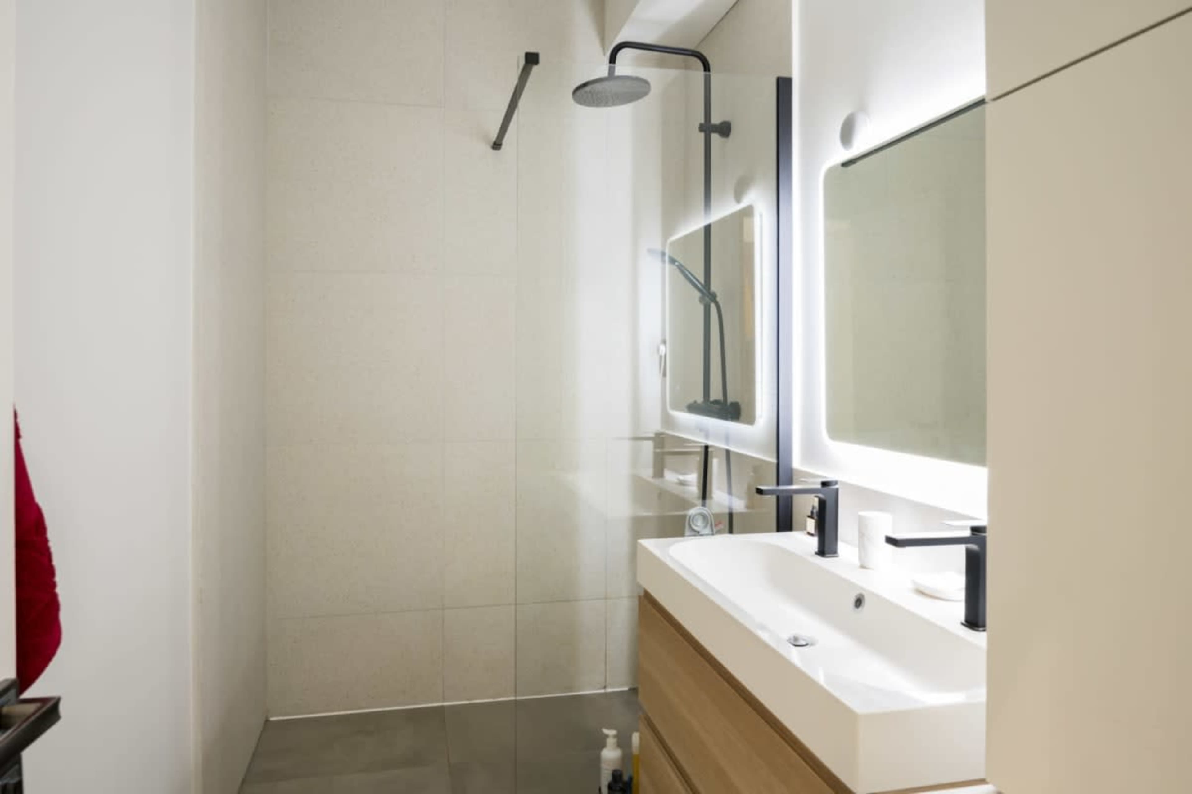 A modern bathroom with a glass shower, a backlit mirror, and a wooden vanity with black fixtures.