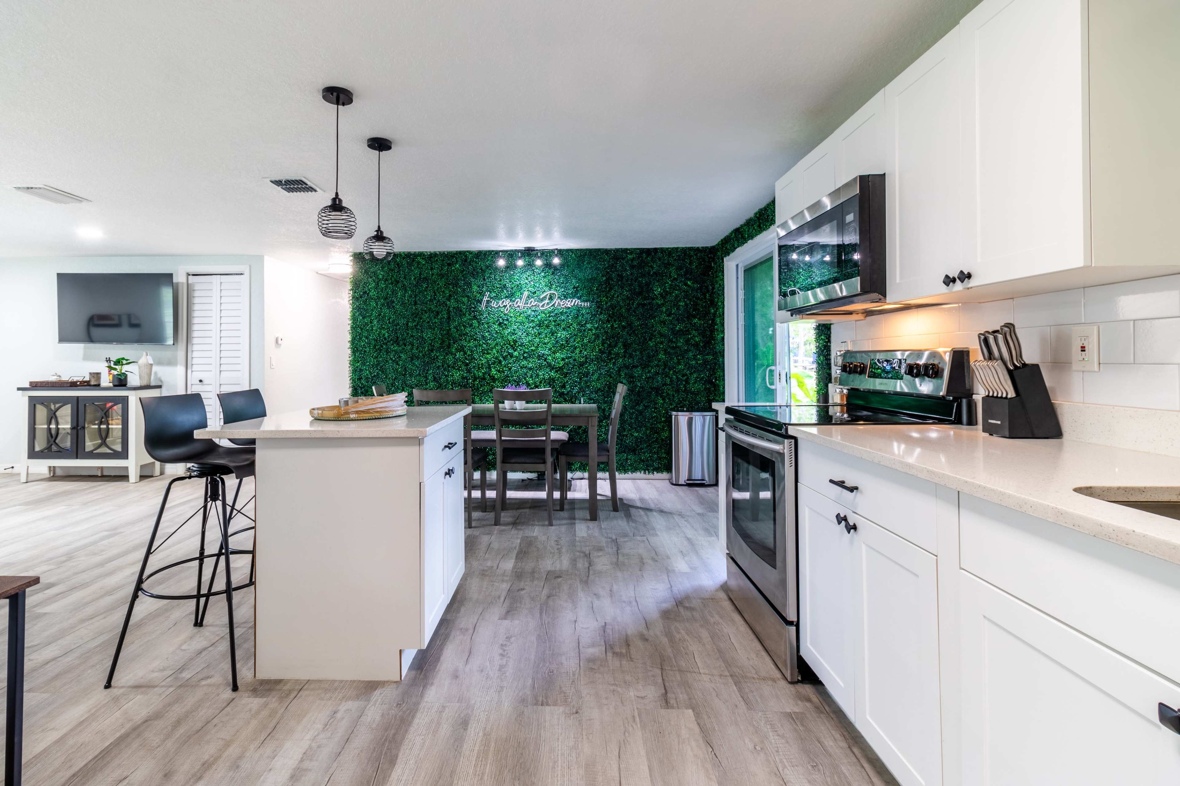 A modern kitchen and dining area with white cabinetry, a countertop, and a green wall feature.