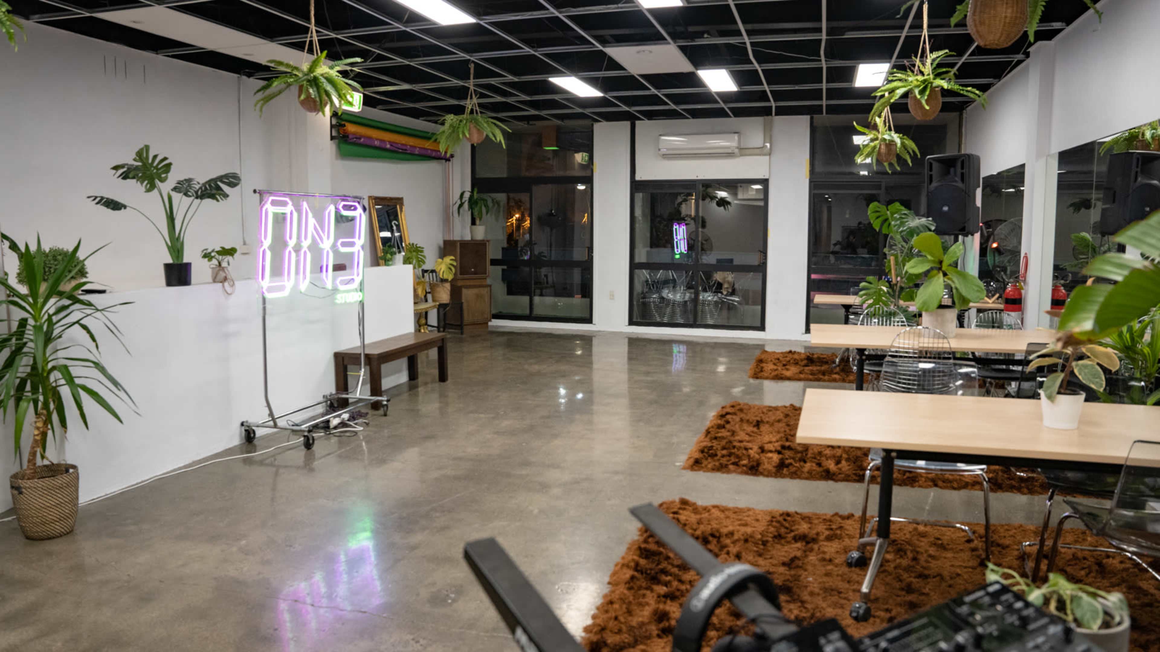 An empty room with a polished concrete floor, two tables, plants in pots, and a neon sign.