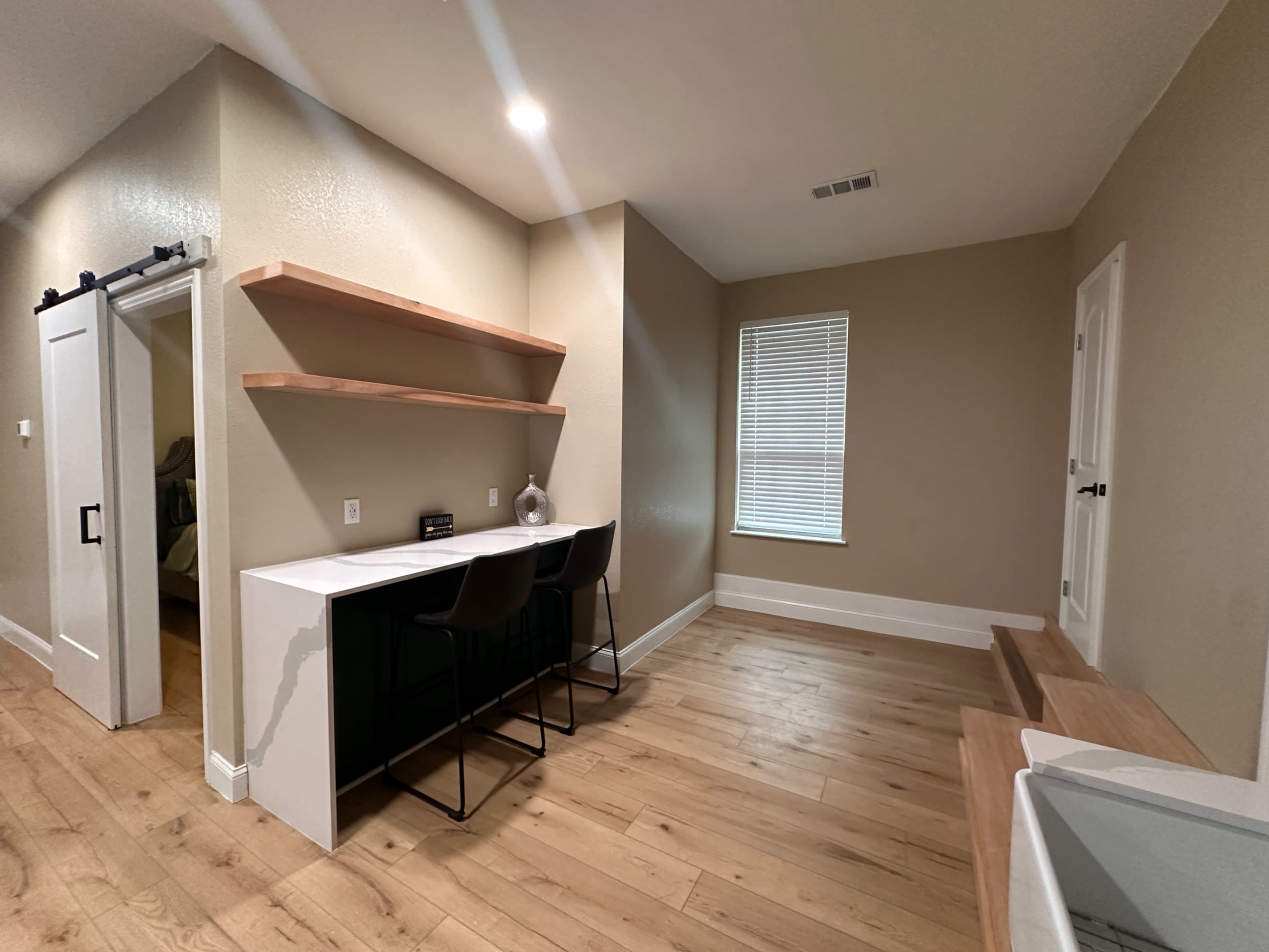 A minimalist interior space with a desk, two shelves, and light-colored wooden flooring.
