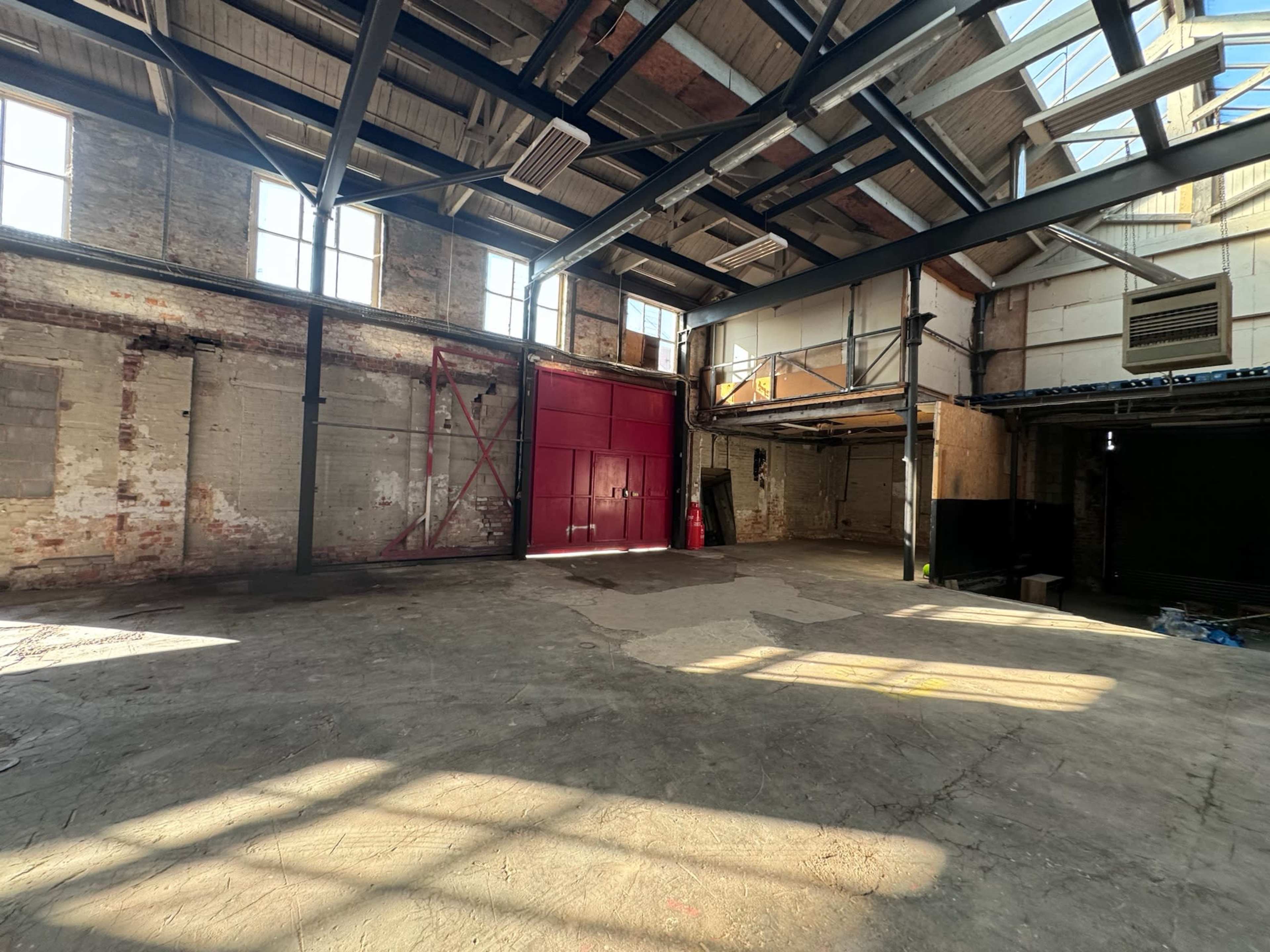 A large, empty industrial space with exposed brick walls, high ceilings, and a red entrance door.