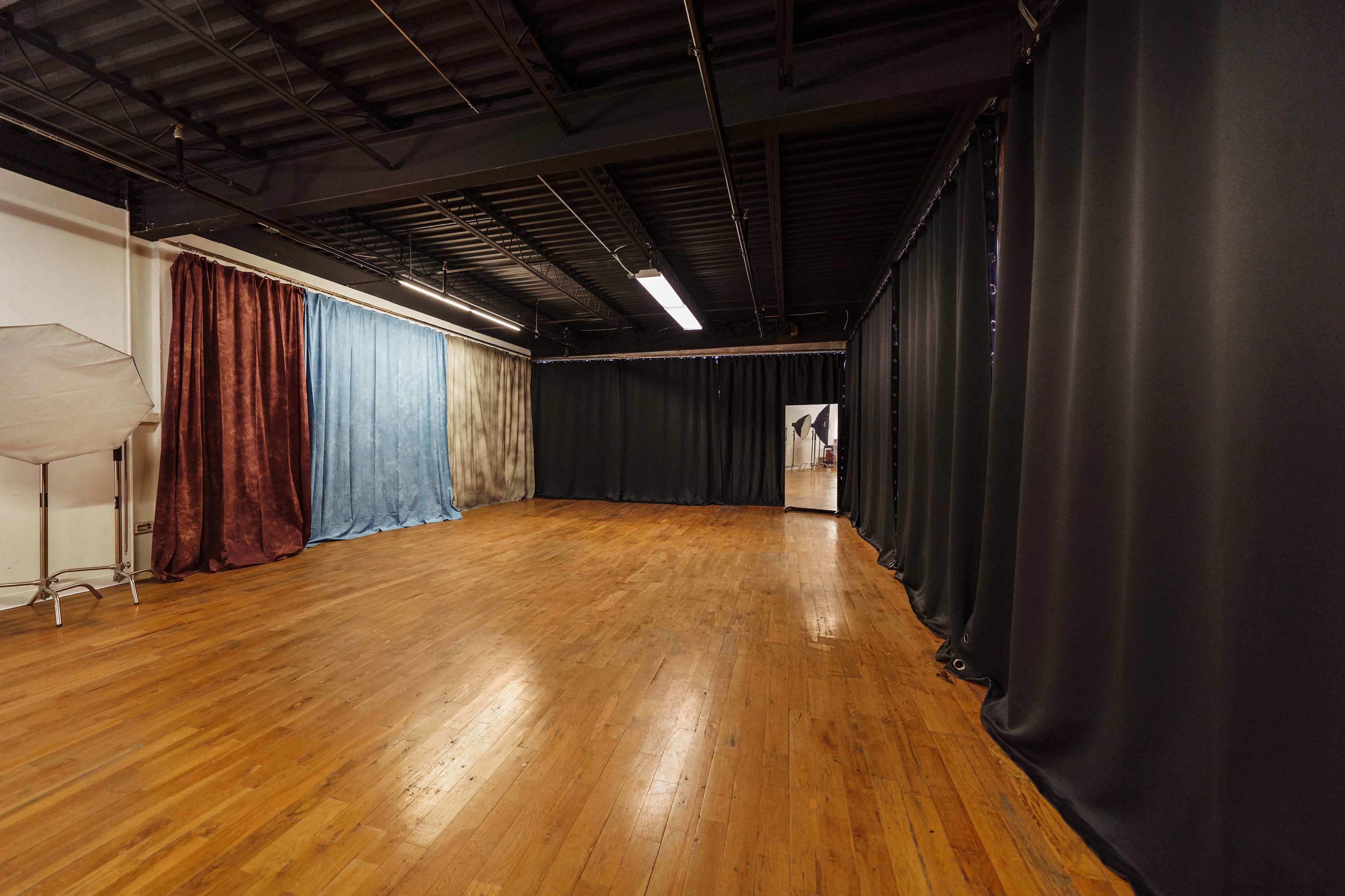 A spacious studio with wooden floors, featuring various backdrops in shades of blue, red, and black, and softly lit by overhead lights.