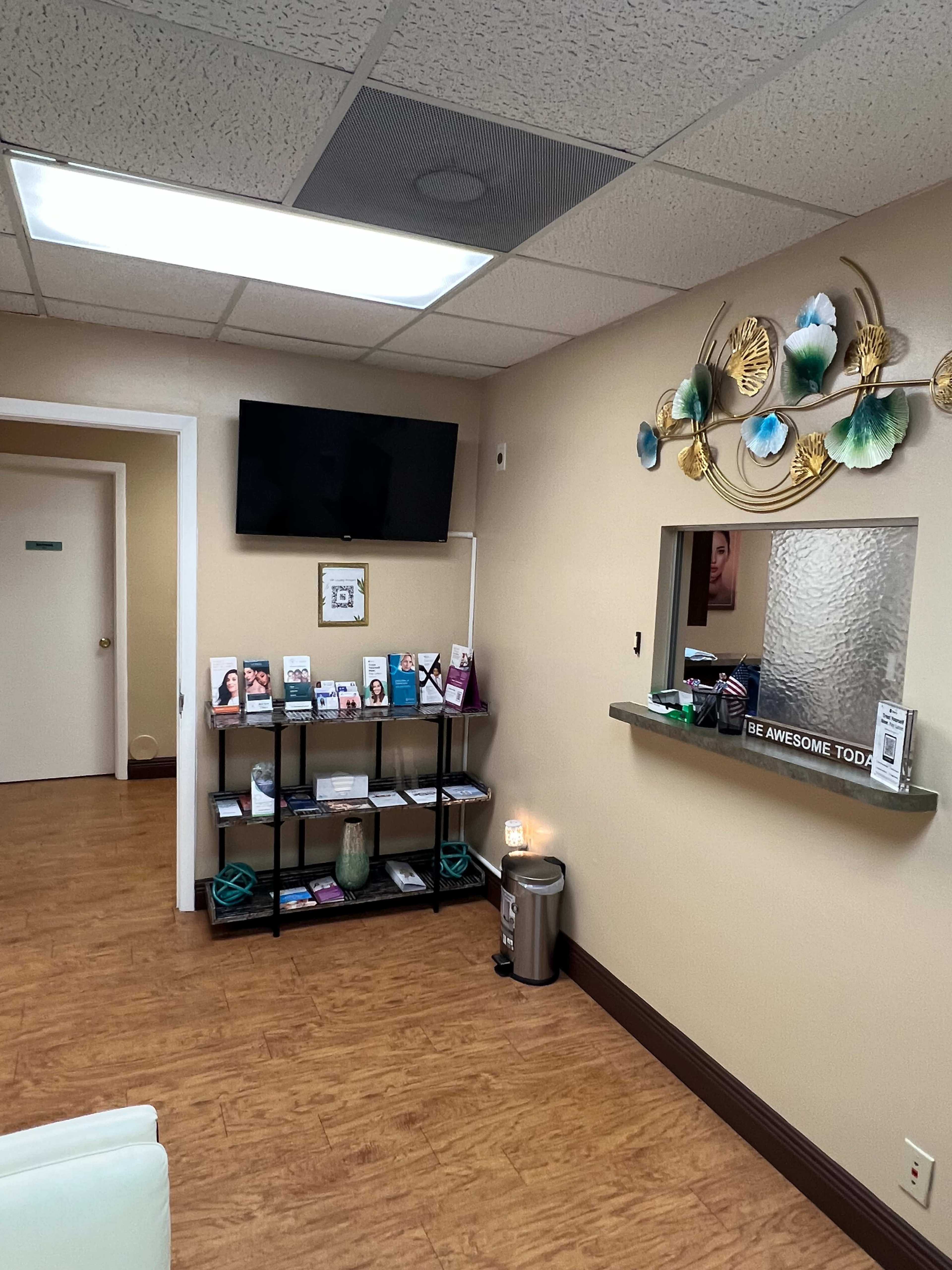 The interior of a waiting area with a television, a bookshelf filled with brochures, and a decorative wall display.