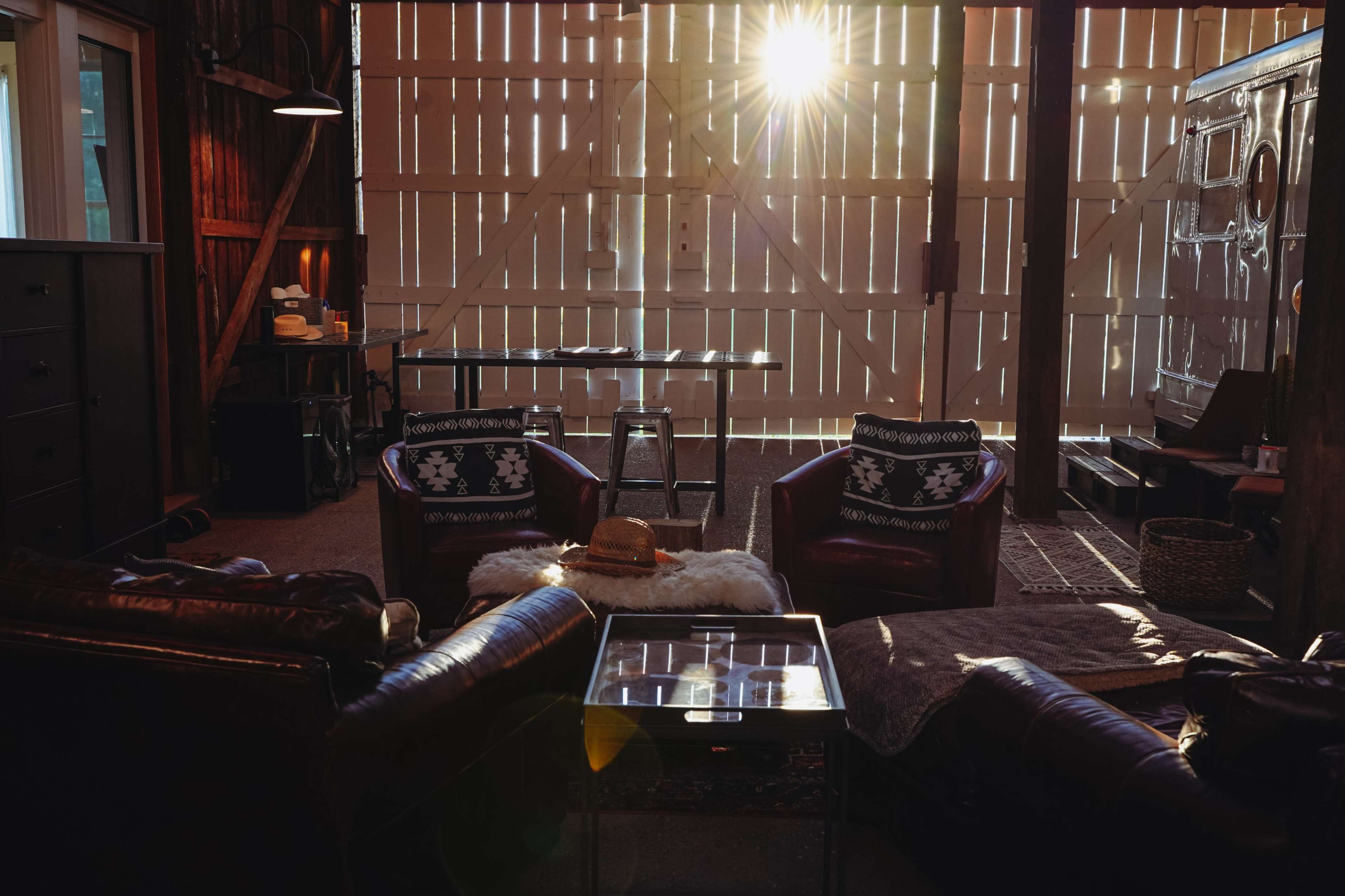 A cozy indoor space features two armchairs, a glass coffee table, and sunlight streaming through slatted wooden doors.