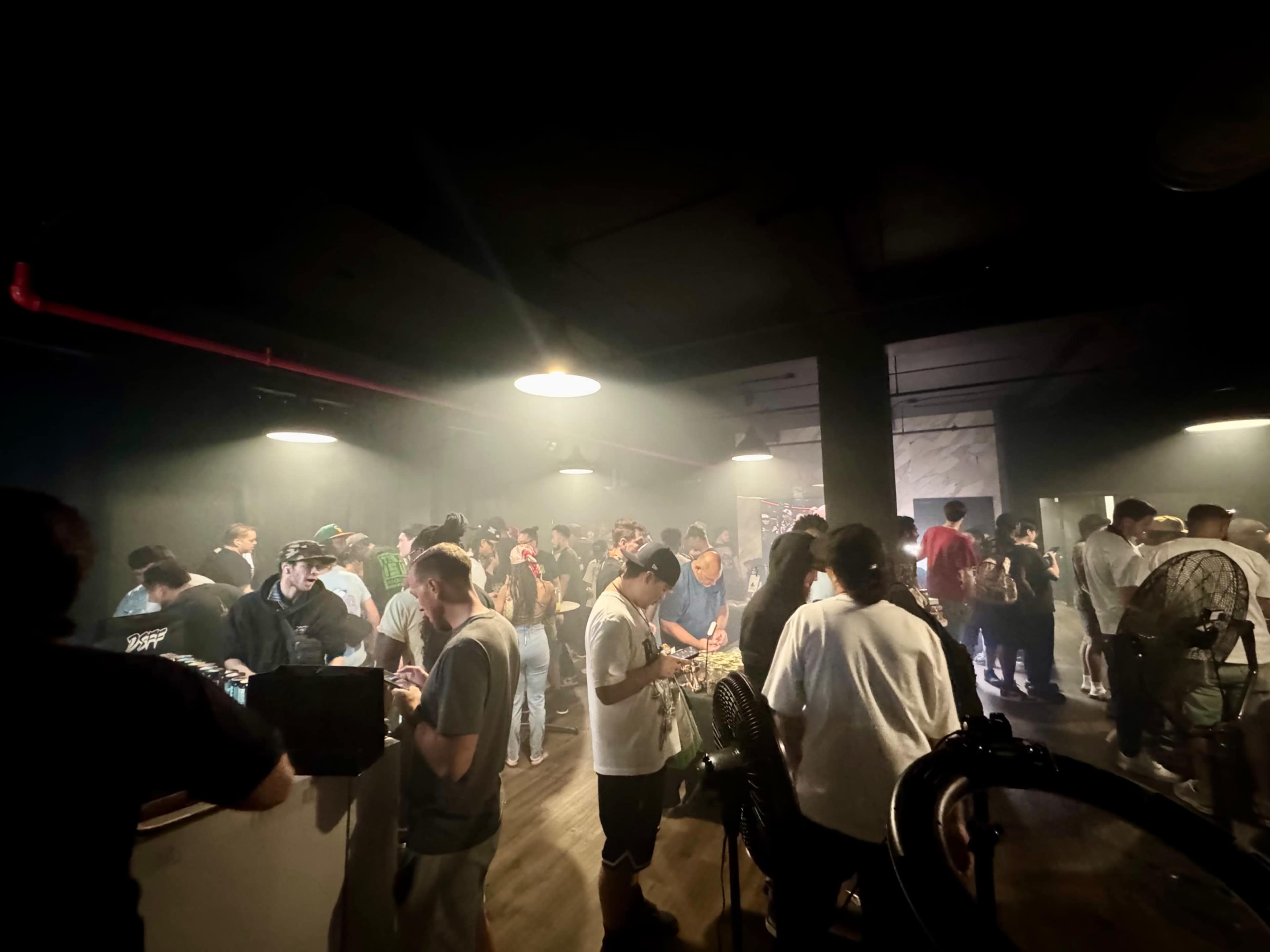A crowded indoor space filled with people socializing under dim lighting and a hazy atmosphere.