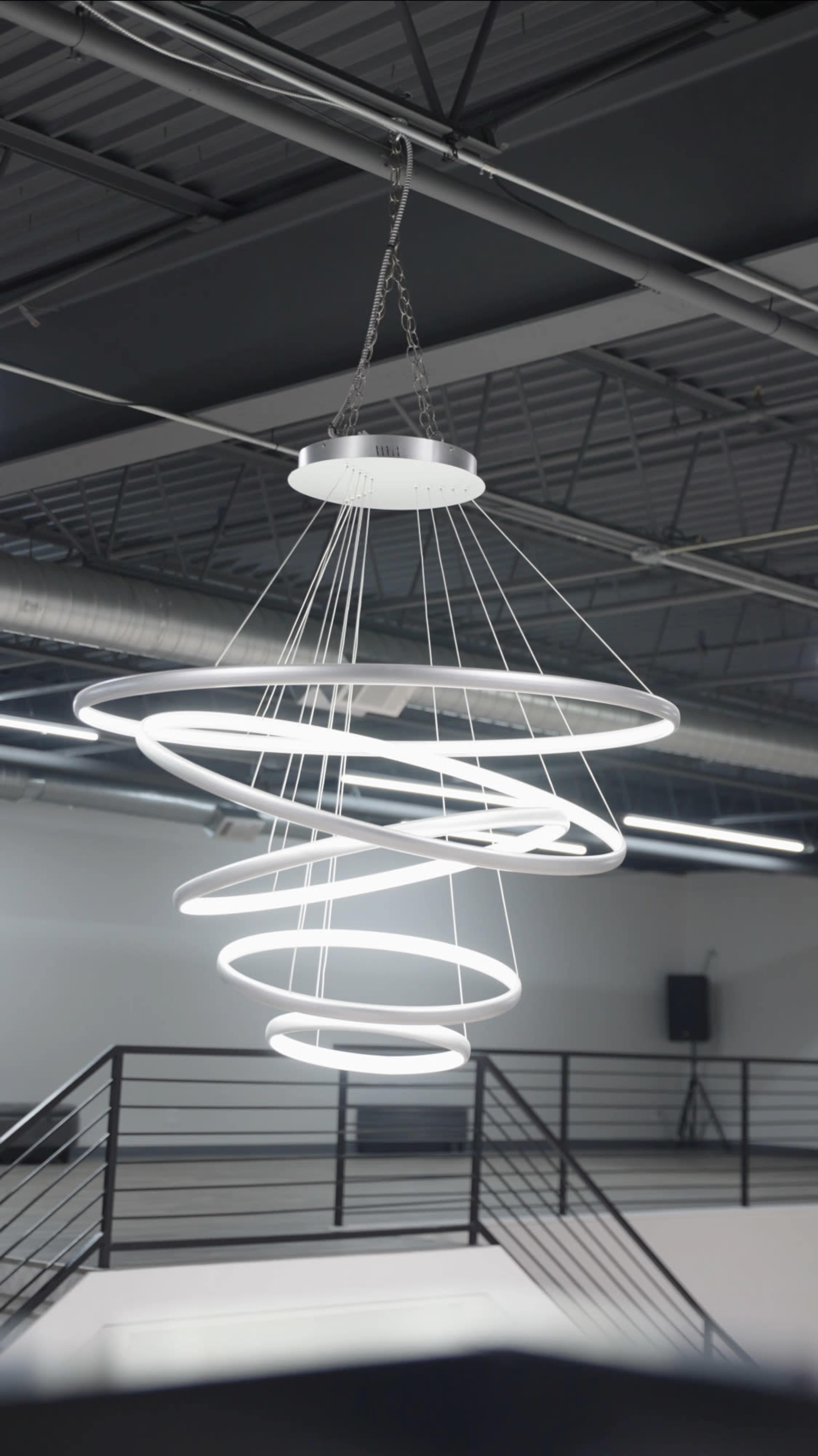 A modern, spiral-shaped LED chandelier hangs from a ceiling in a spacious interior space.