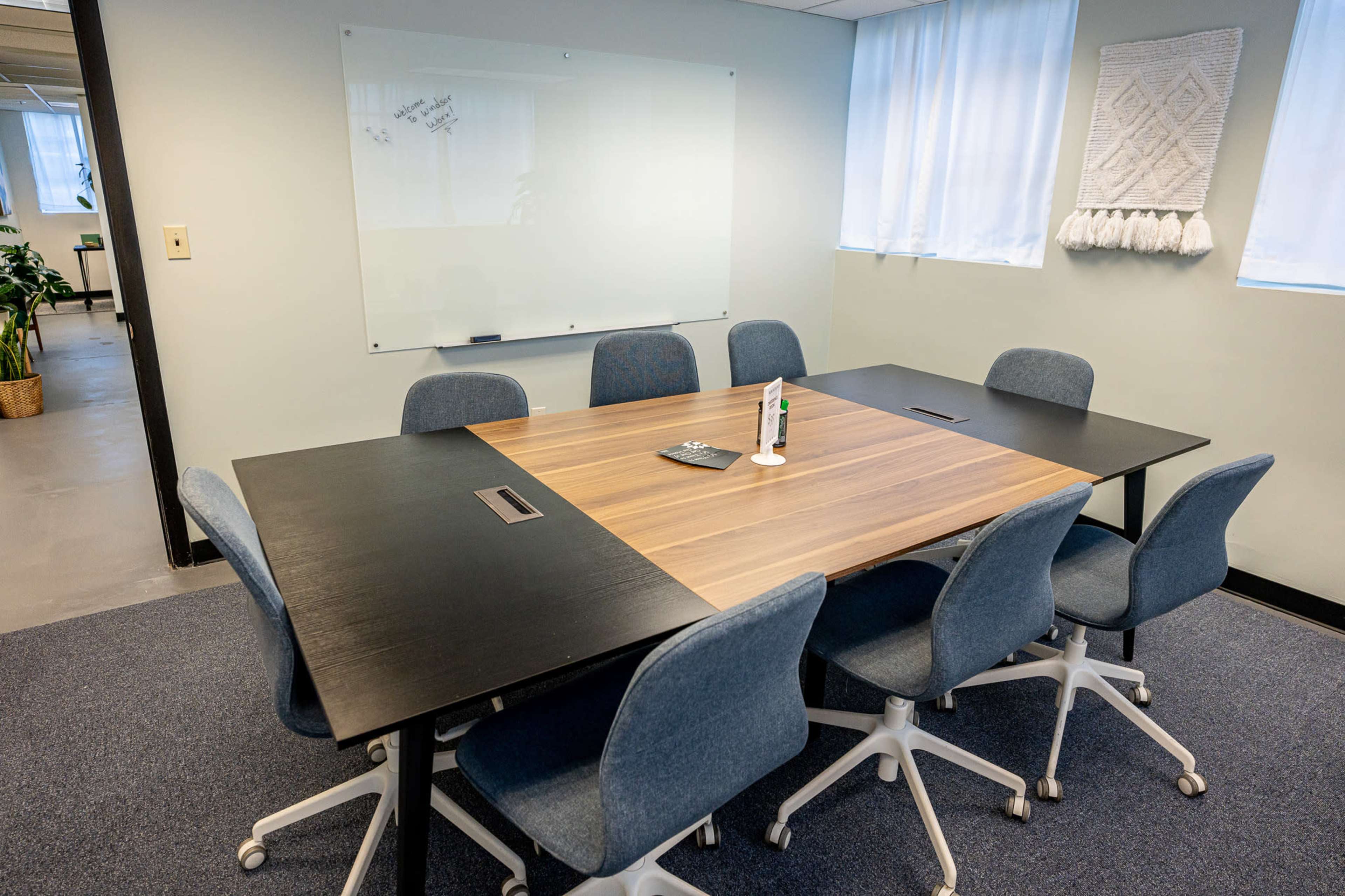 A conference room features a large wooden table surrounded by gray swivel chairs and a whiteboard on the wall.