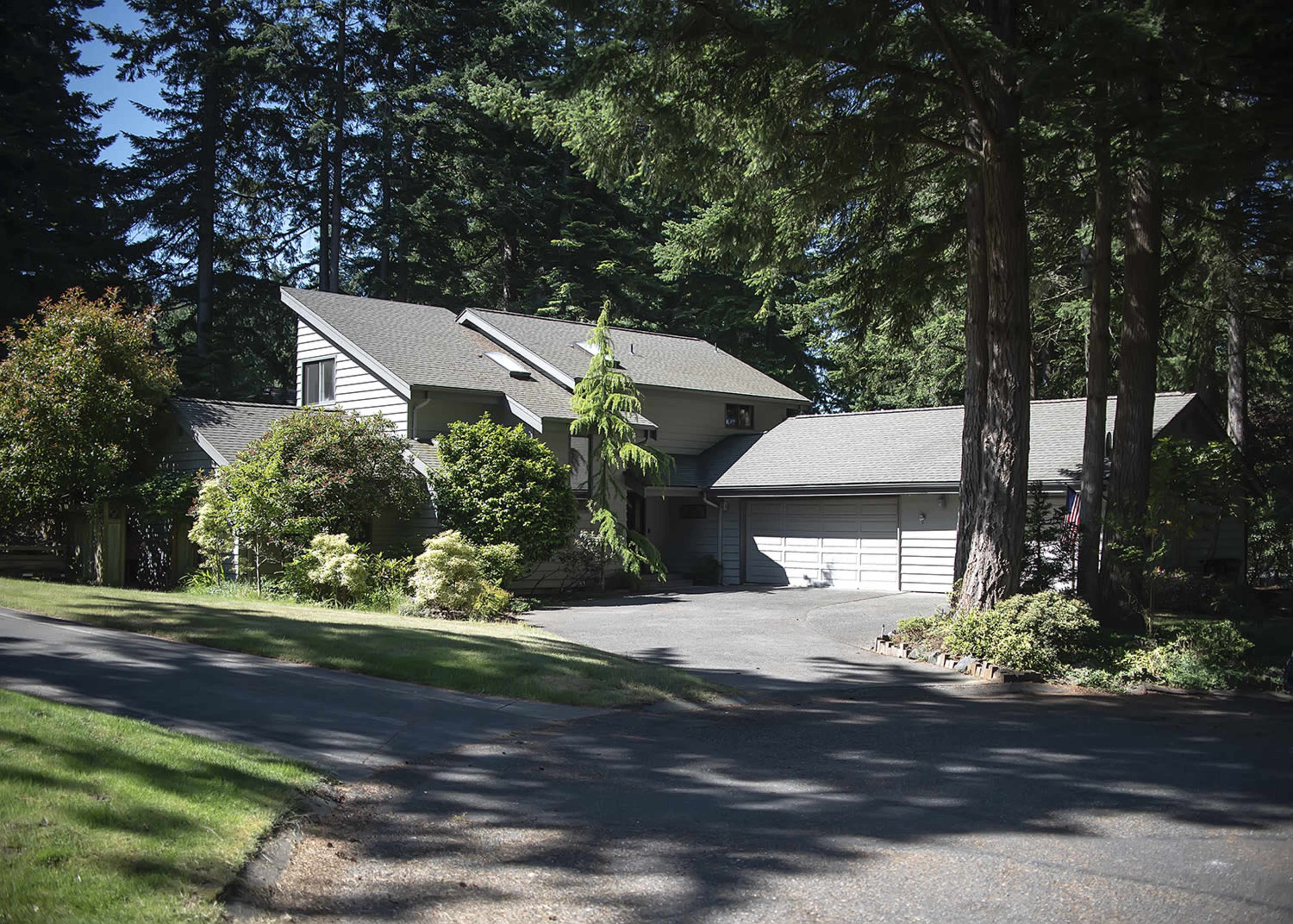 A two-story house with a garage is surrounded by trees and landscaped gardens.