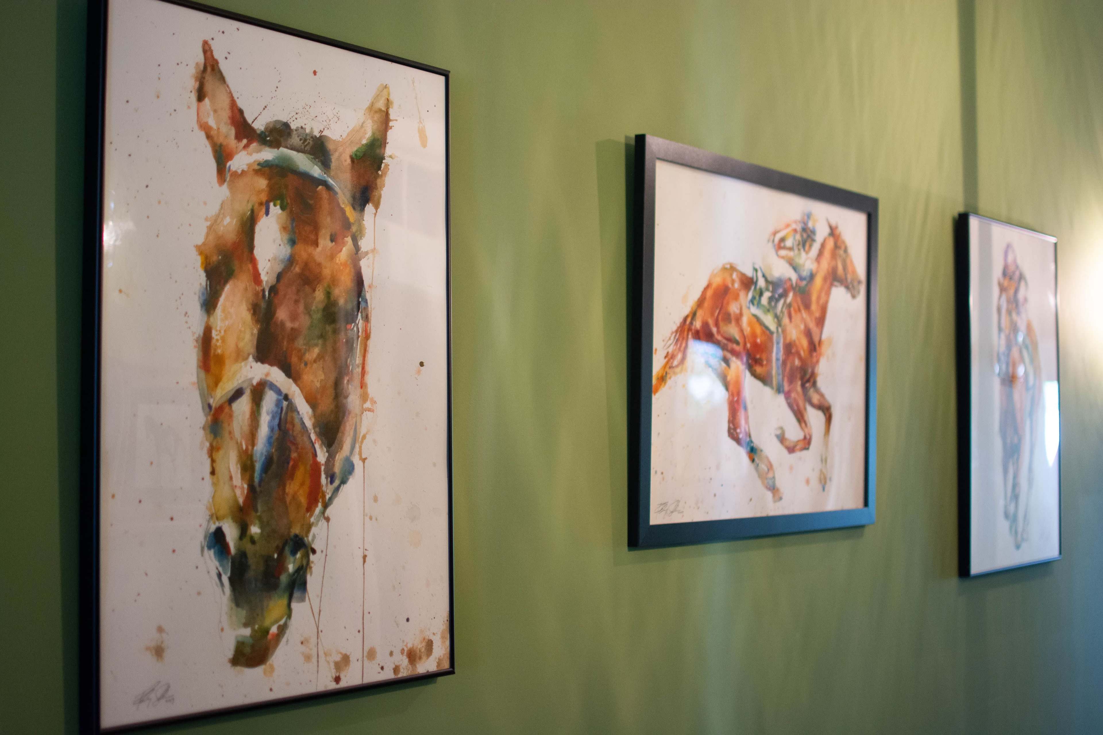 Three framed watercolor paintings of horses are displayed on a green wall.
