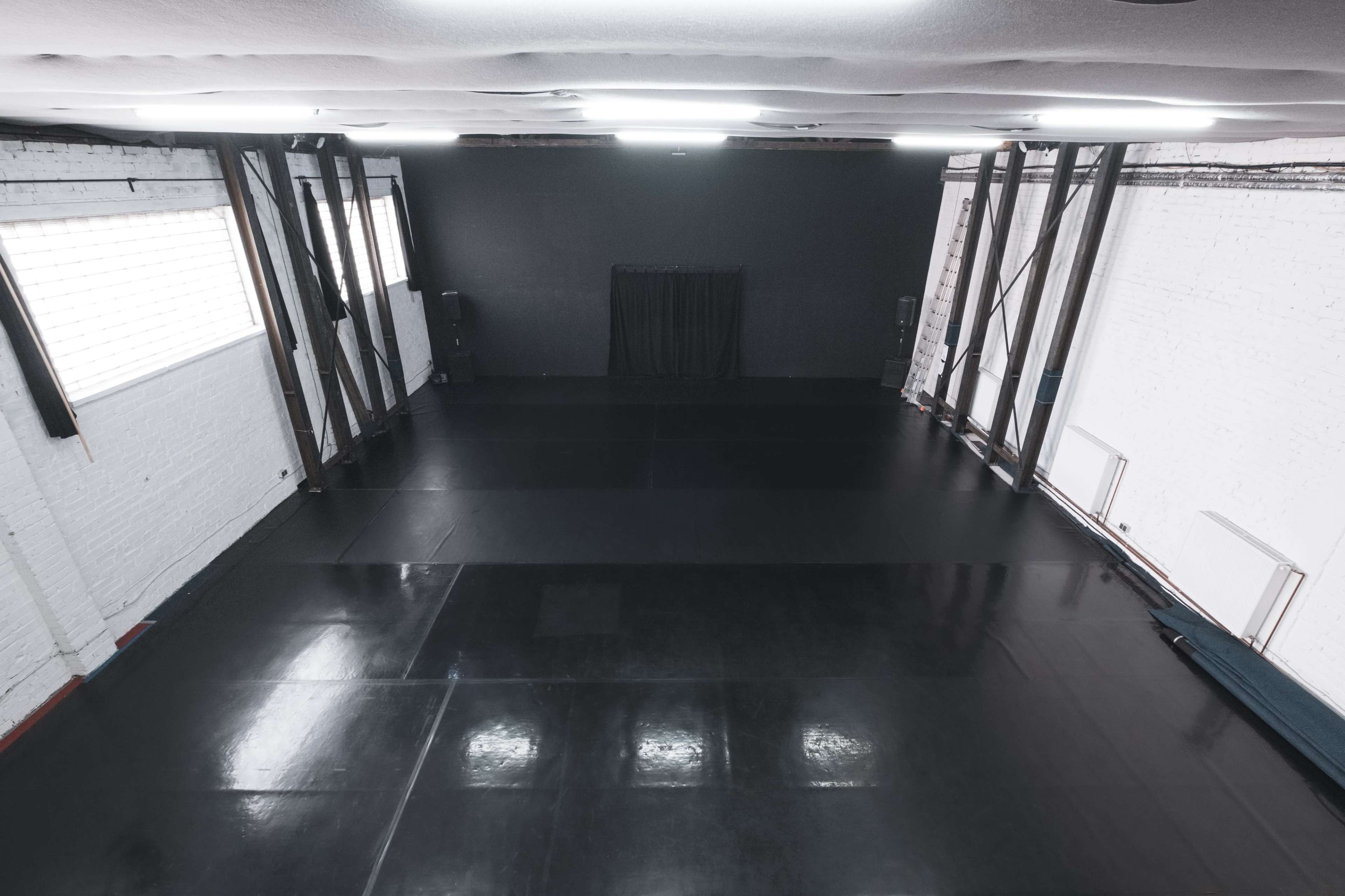 A spacious, empty room with a polished black floor and industrial-style walls.