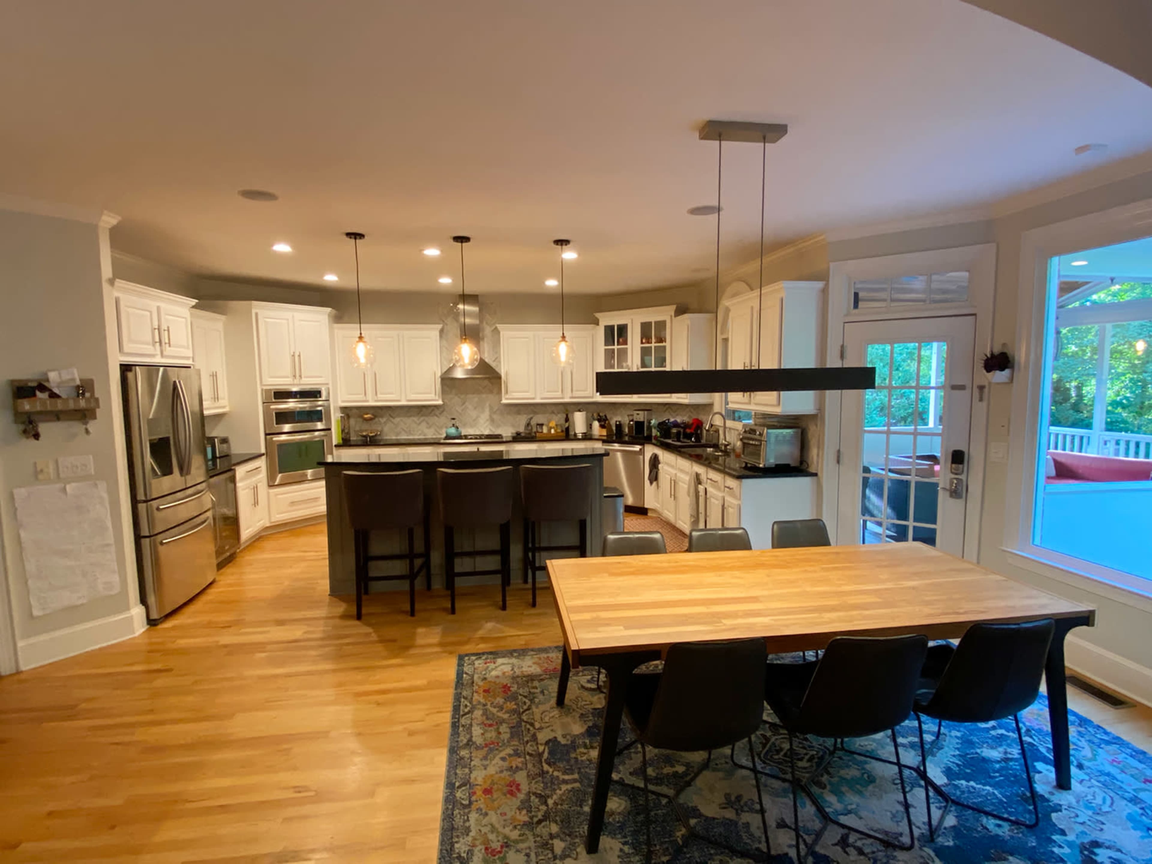 A modern kitchen with white cabinetry, stainless steel appliances, and a central island with bar seating, adjacent to a dining table surrounded by six chairs.