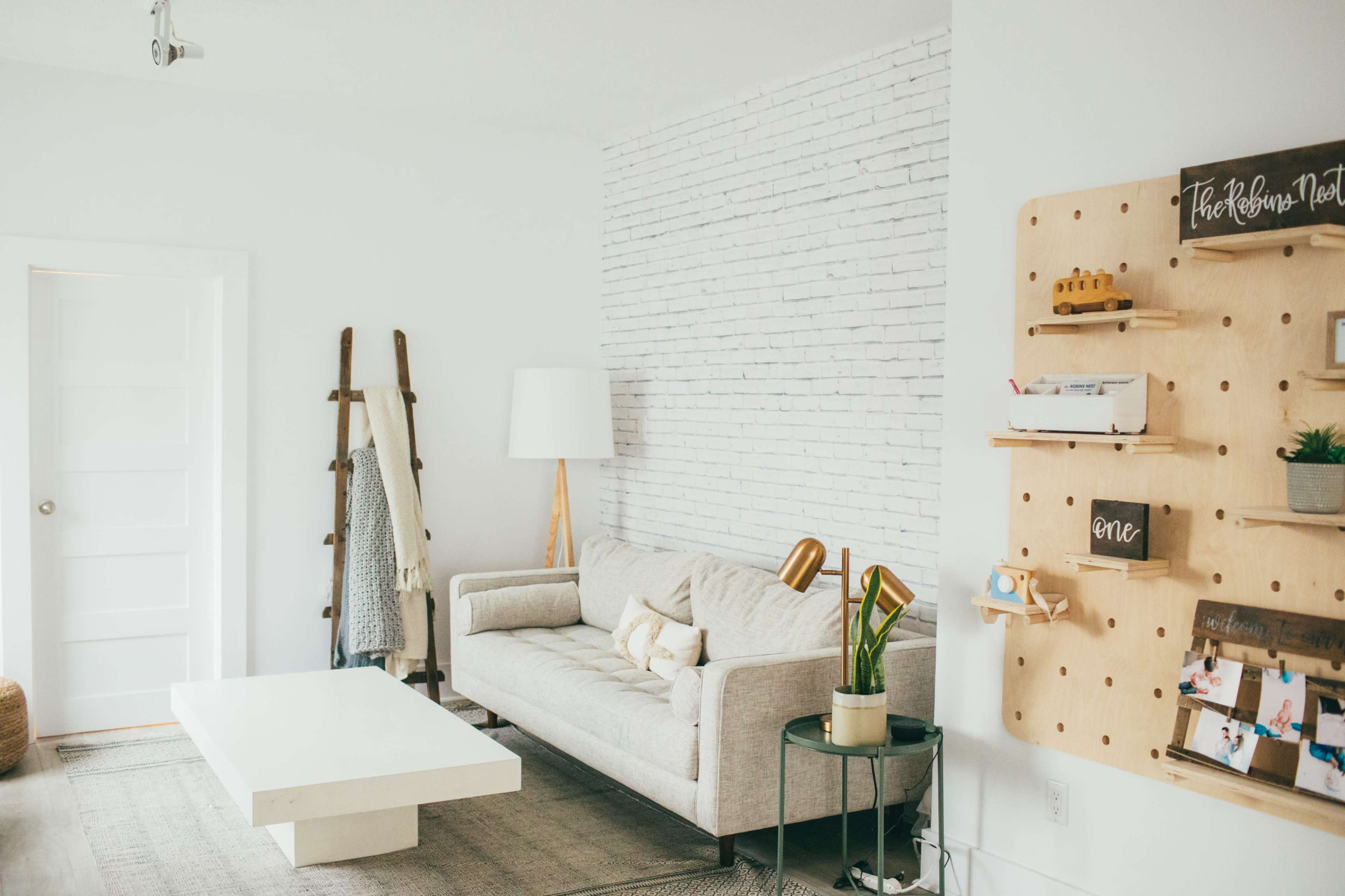 A modern living room features a light gray sofa, a white coffee table, a floor lamp, and a wall-mounted display with shelves and decorations.
