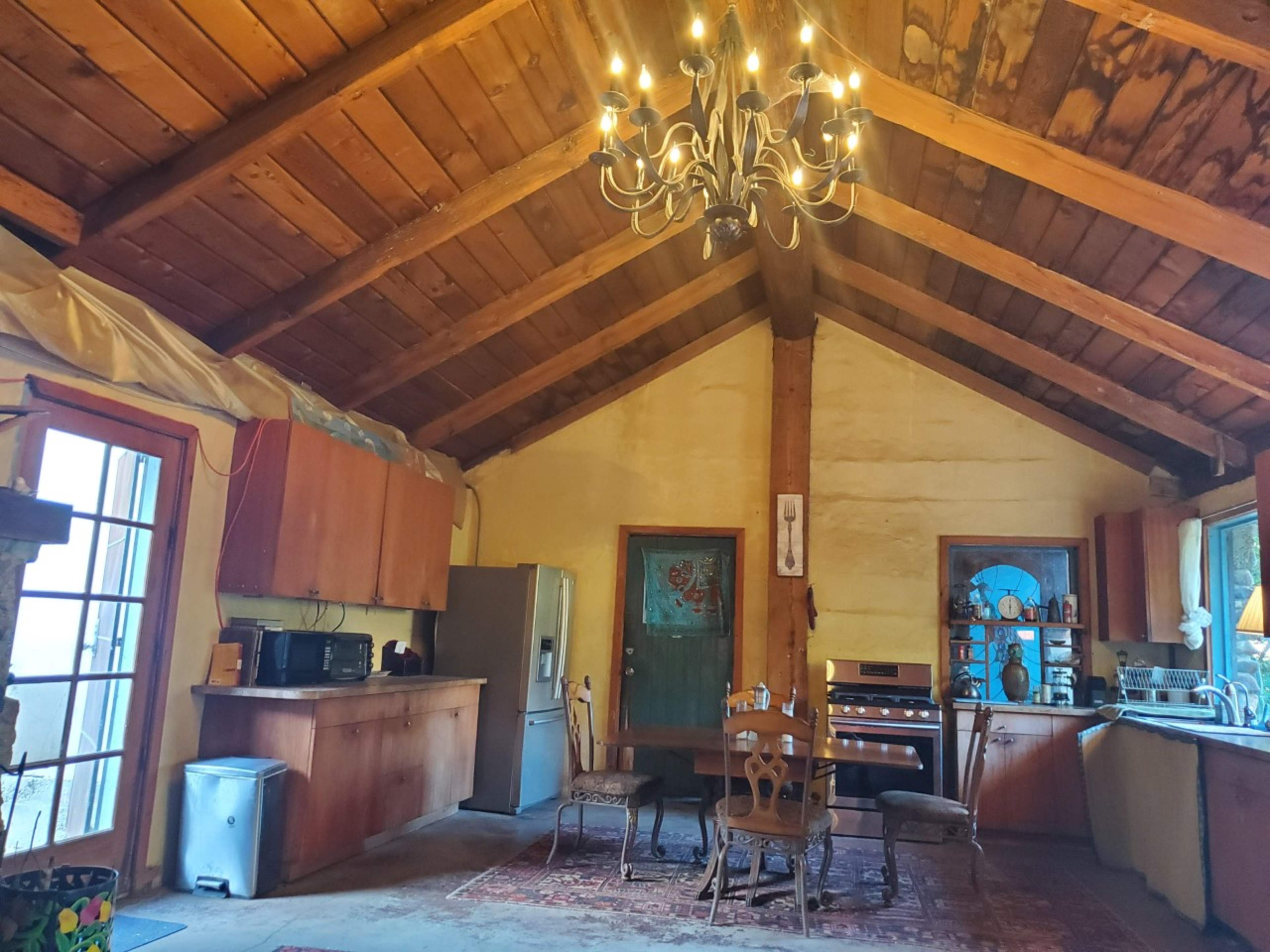 A rustic kitchen with wooden beams, a chandelier, and a dining table accompanied by chairs.