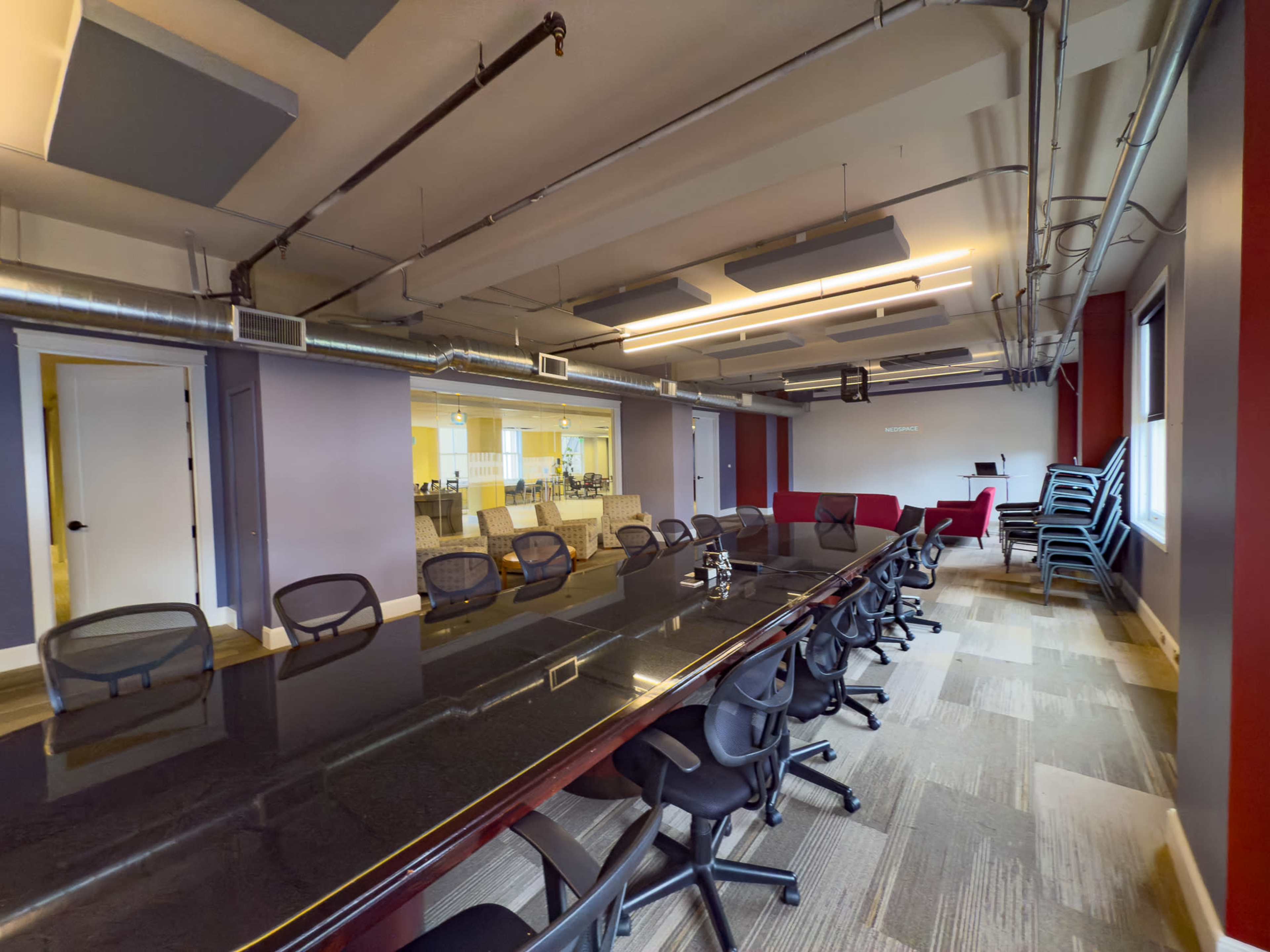 The image shows a spacious conference room with a long table surrounded by black chairs, and a view of an adjacent room through glass panels.