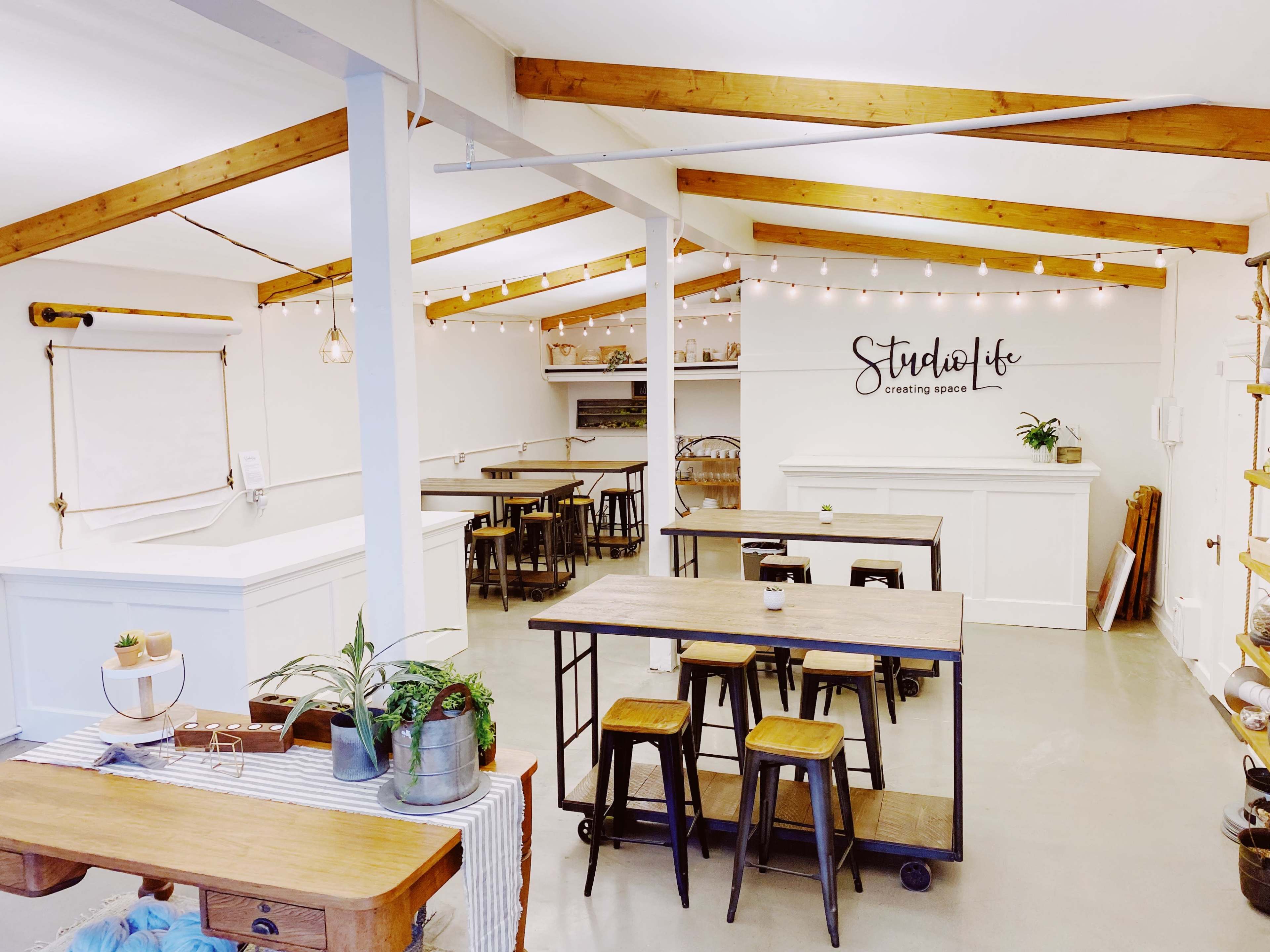 A spacious, well-lit studio with wooden beams, several tables, and stools arranged in a clean, minimalist layout.