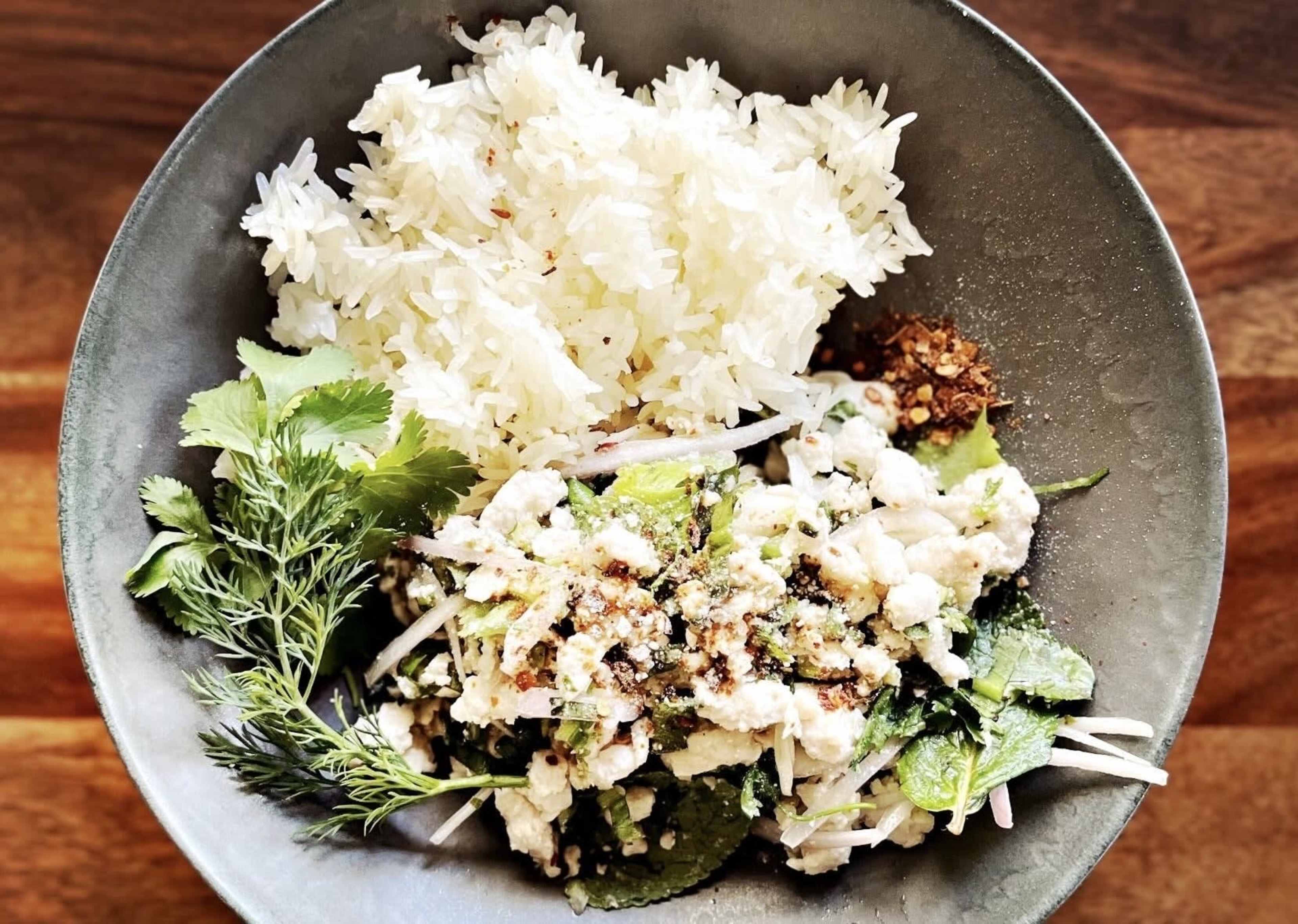 A bowl contains white rice alongside a dish of minced chicken mixed with herbs and garnished with spices.