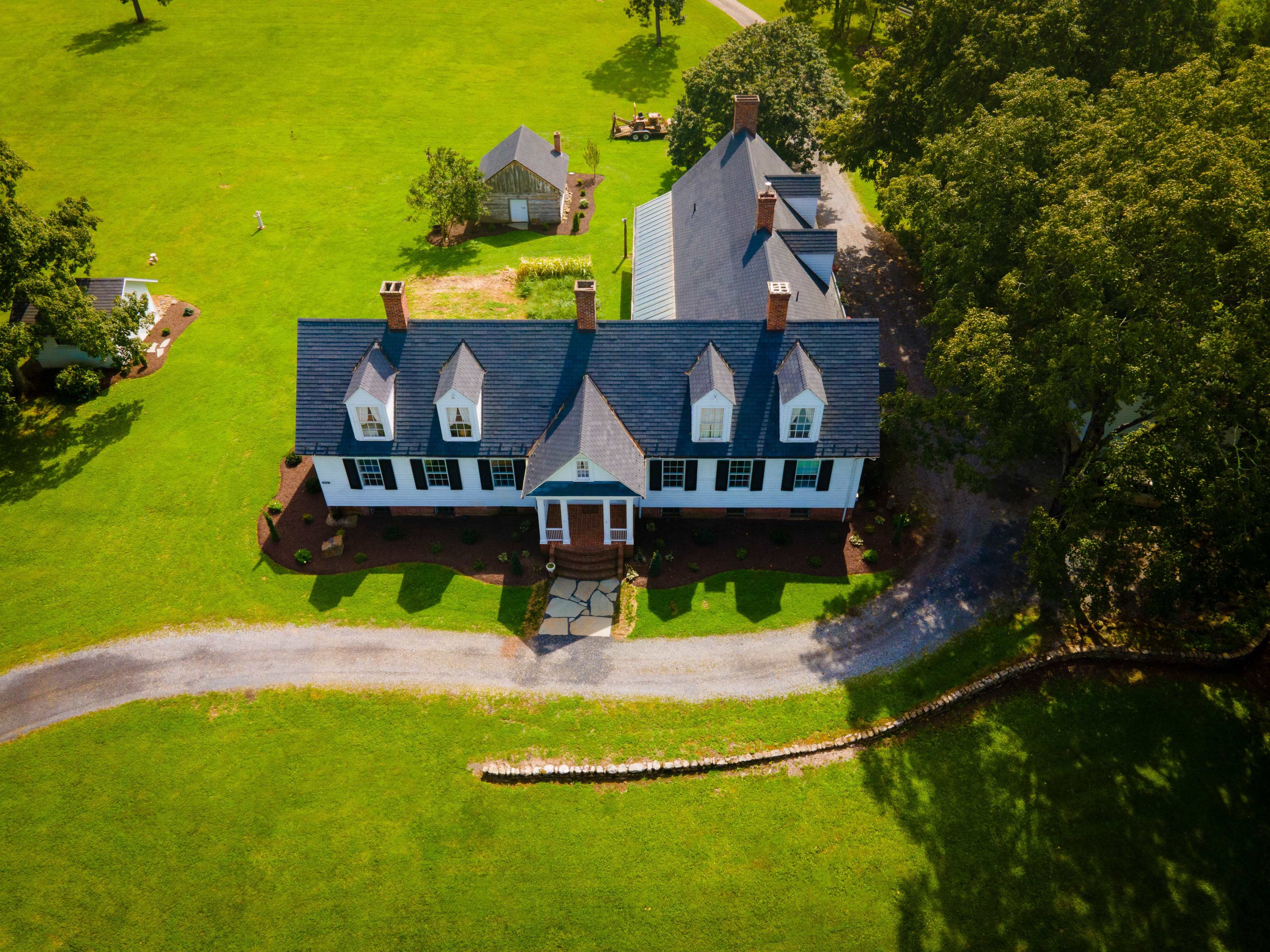 A large, two-story white house with a dark blue roof situated on a green lawn, with a gravel path leading up to the entrance.