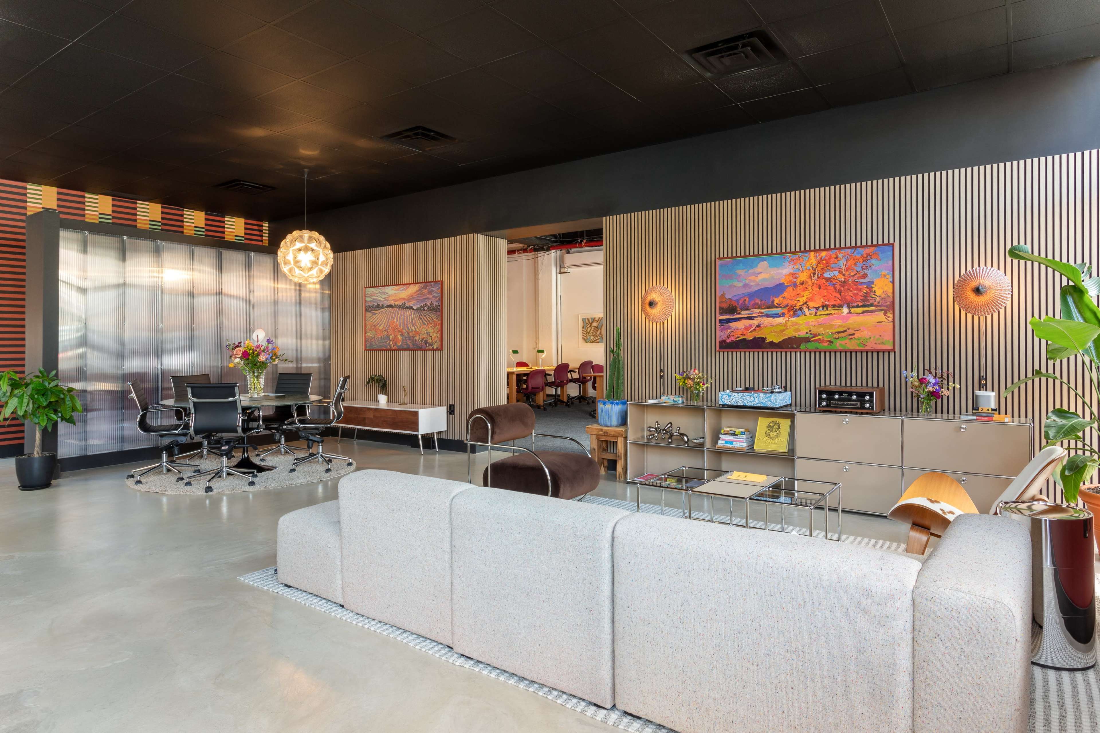 The image shows a modern office interior featuring a mix of seating areas, artwork on the walls, and a conference table in a spacious, open layout.