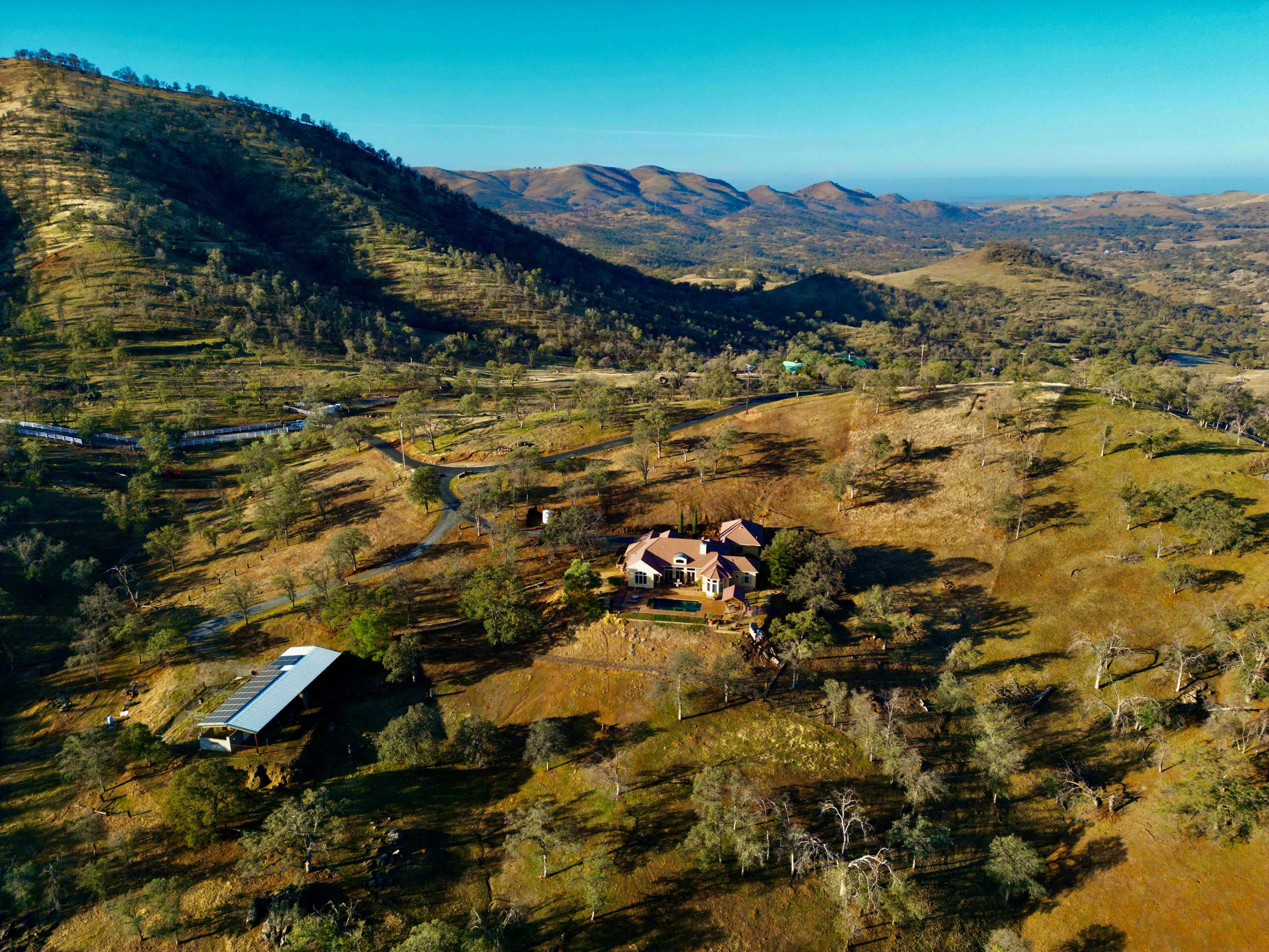 A large house surrounded by rolling hills and scattered trees in a rural landscape.