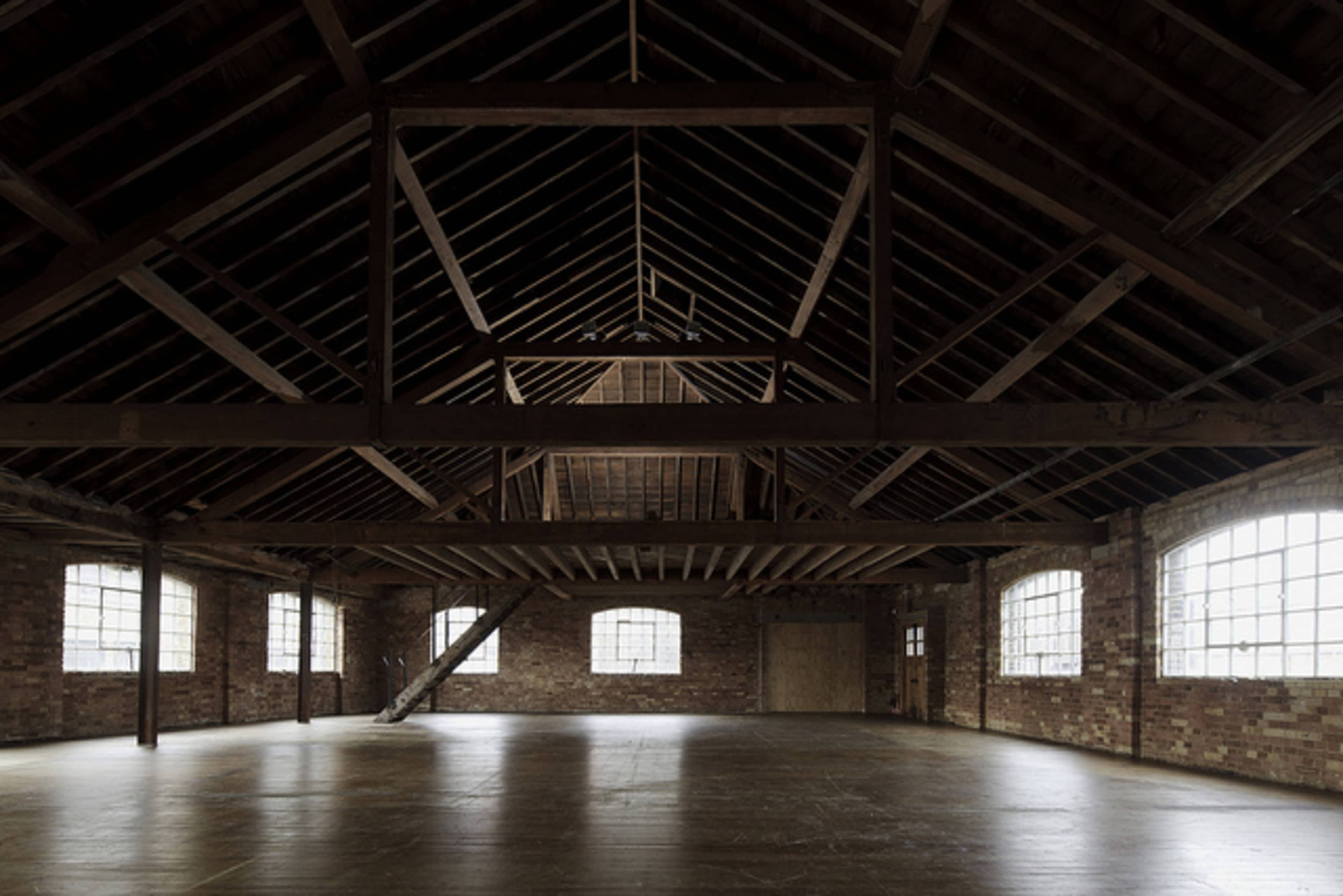 An empty, industrial-style loft with wooden beams and large windows.