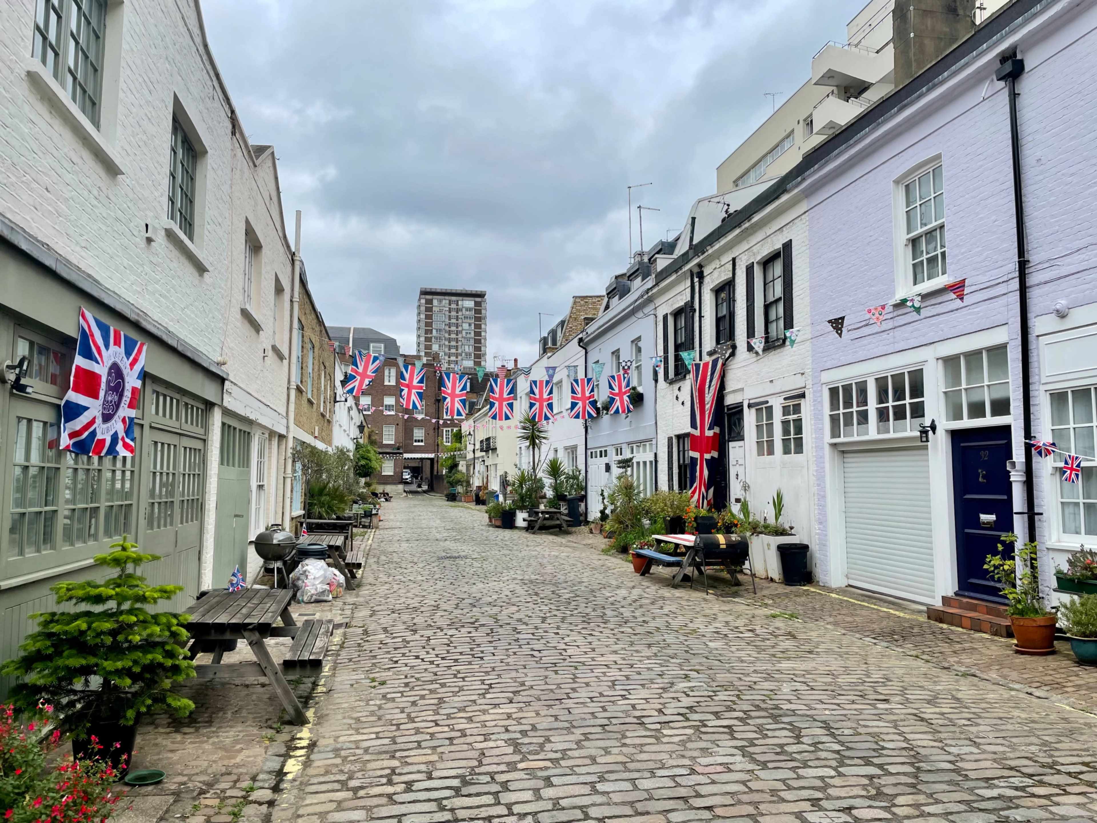 A cobblestone street lined with white and pastel-colored buildings is decorated with Union Jack flags and bunting.