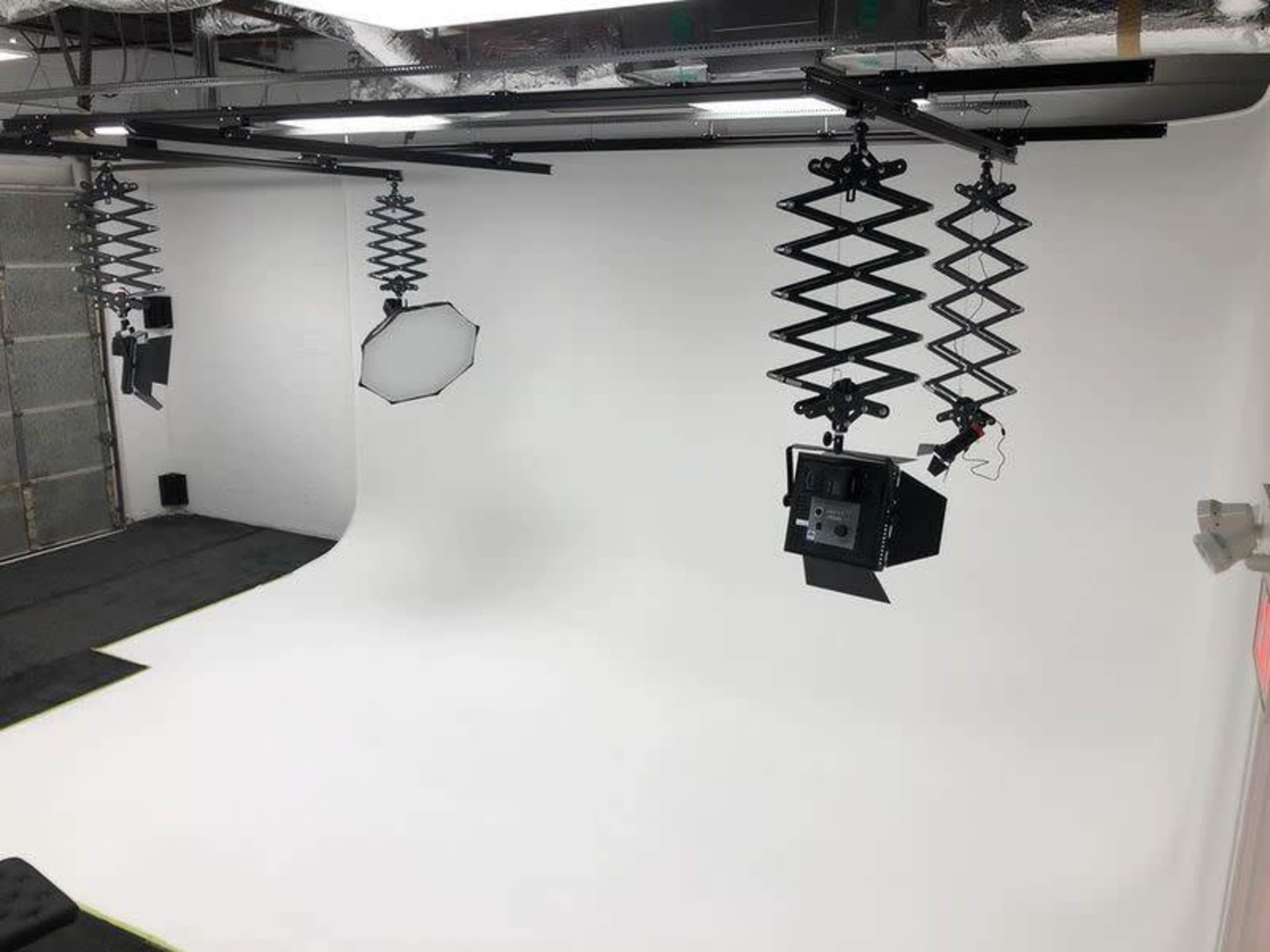 A photography studio with a seamless white backdrop and hanging lights on adjustable stands.
