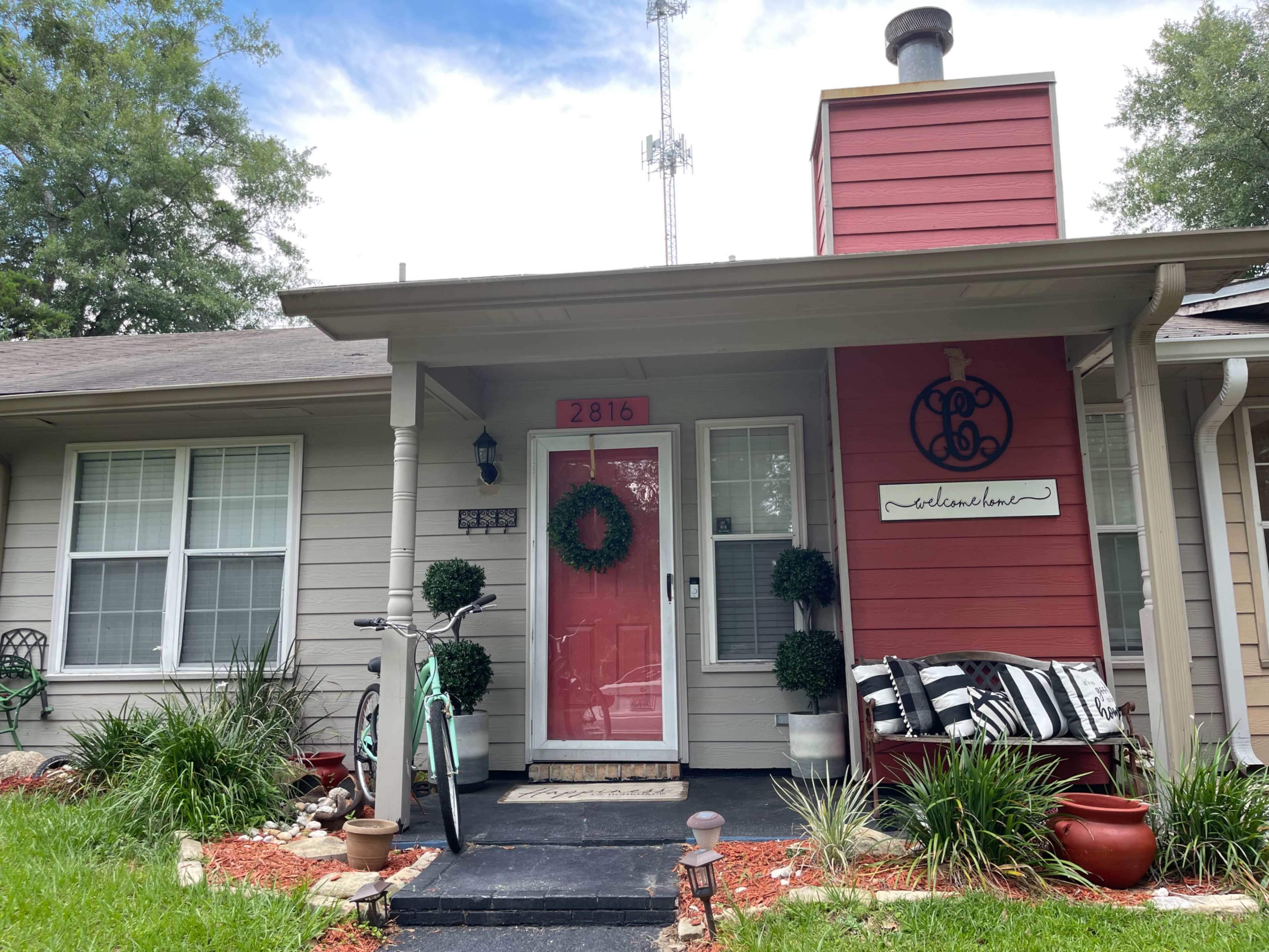 A house with a red door, a decorative sign, and a bicycle parked on the left side of the porch.