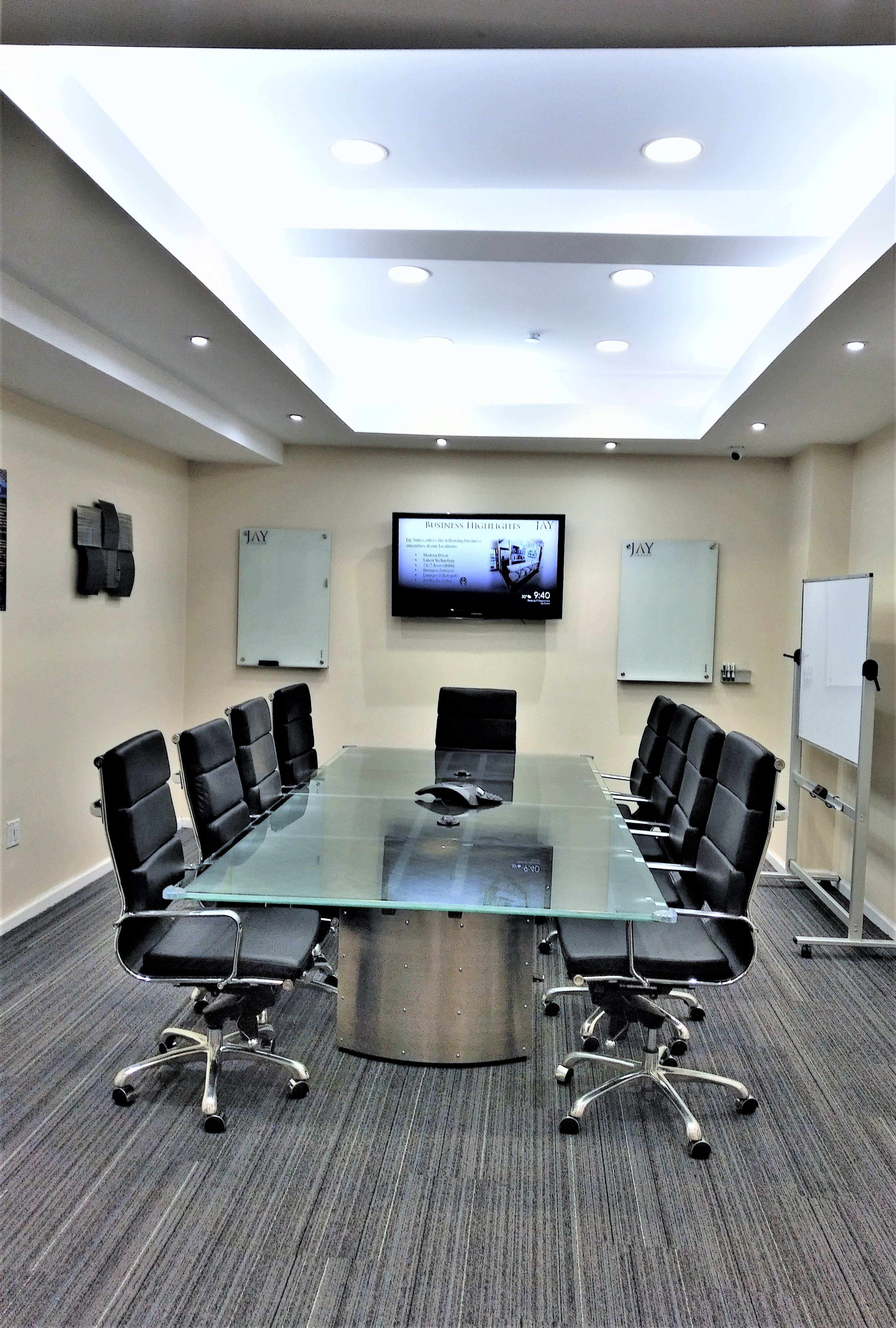 A modern conference room with a glass table surrounded by black chairs and equipped with a large screen display on the wall.