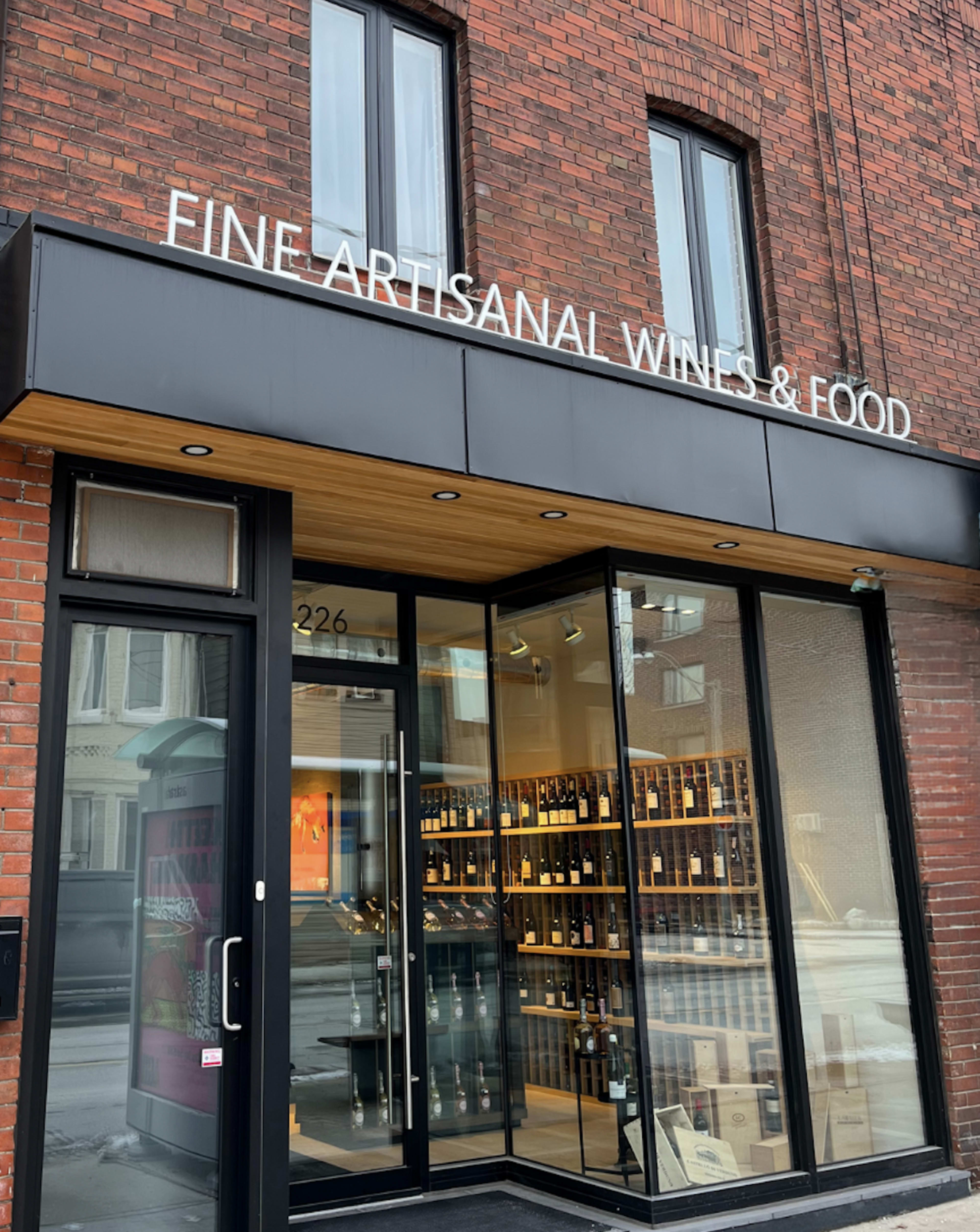 The entrance of a wine and food shop features large glass doors and a sign that reads "FINE ARTISANAL WINES & FOOD" above the doorway.