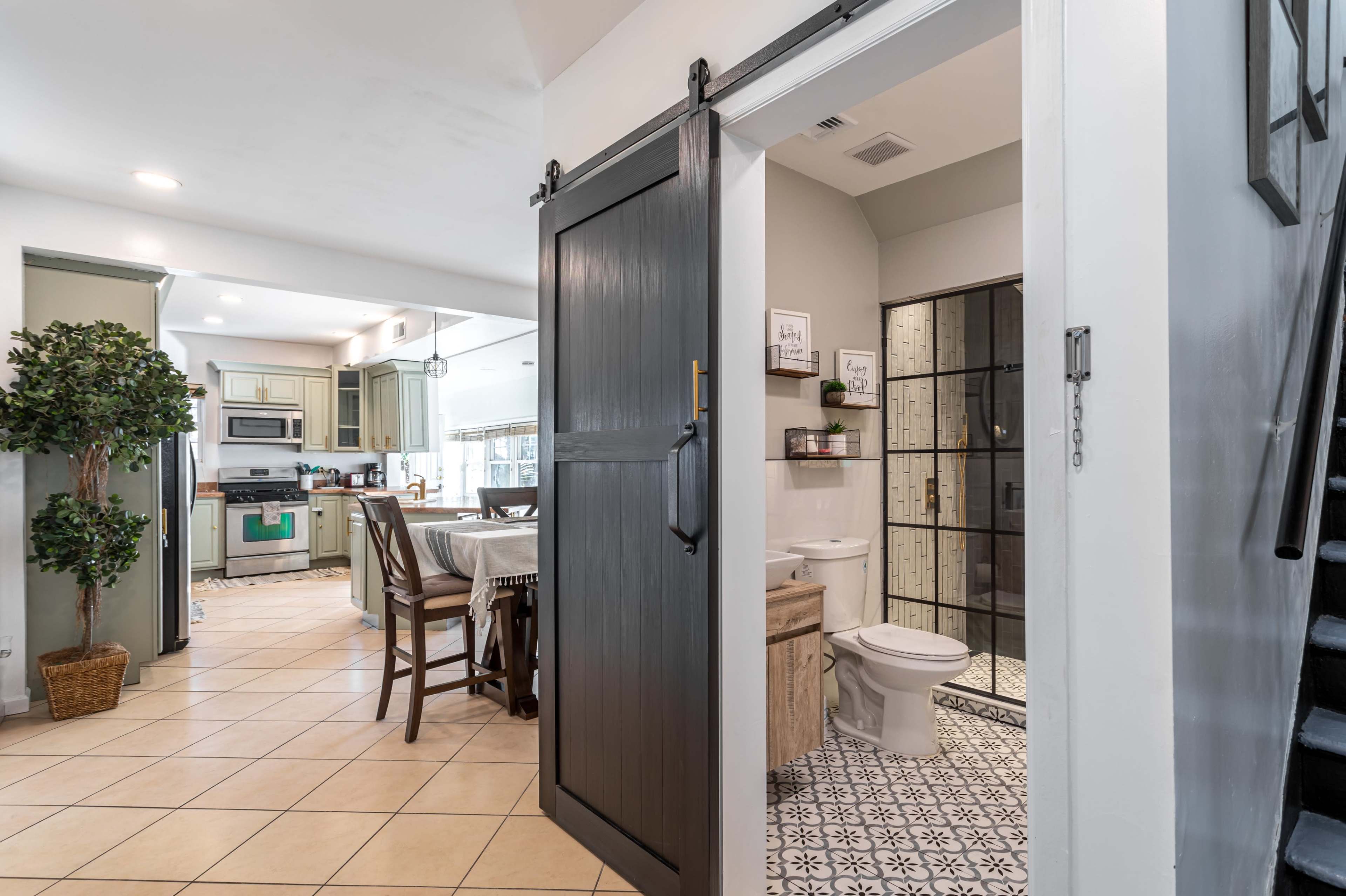 An entryway with a sliding barn door that leads to a bathroom, adjacent to a dining area with a table and chairs, and a visible kitchen in the background.