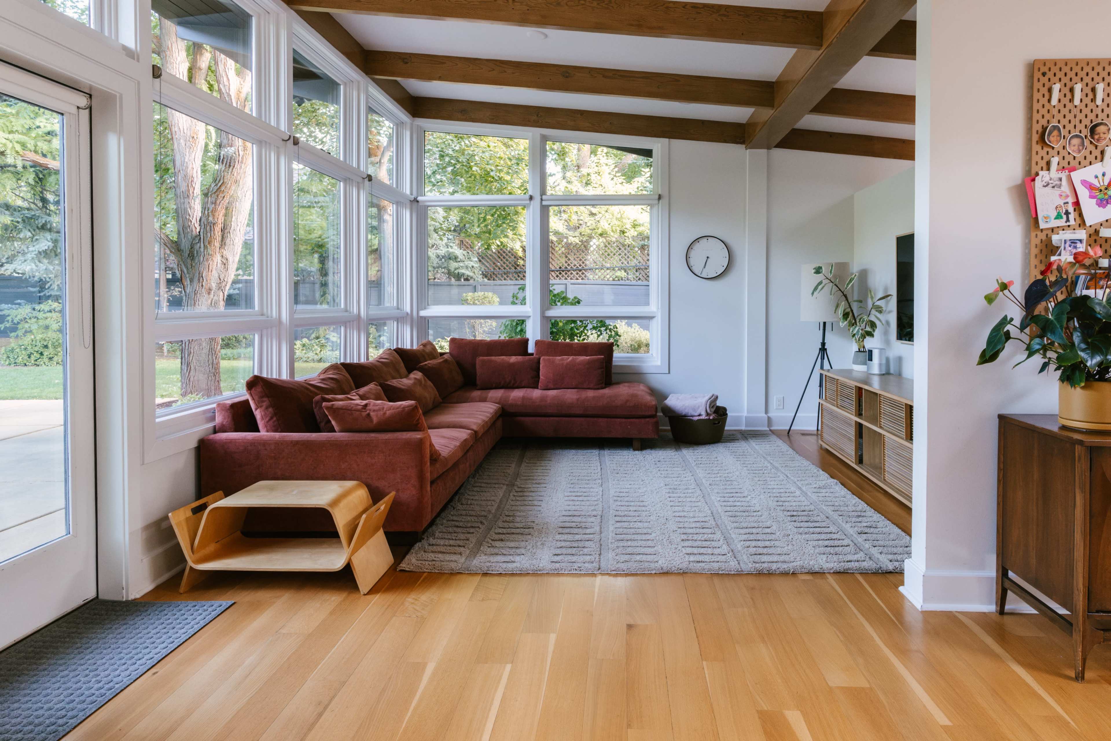 The image shows a modern living room with a large sectional sofa, wooden beams, and large windows allowing natural light to enter.