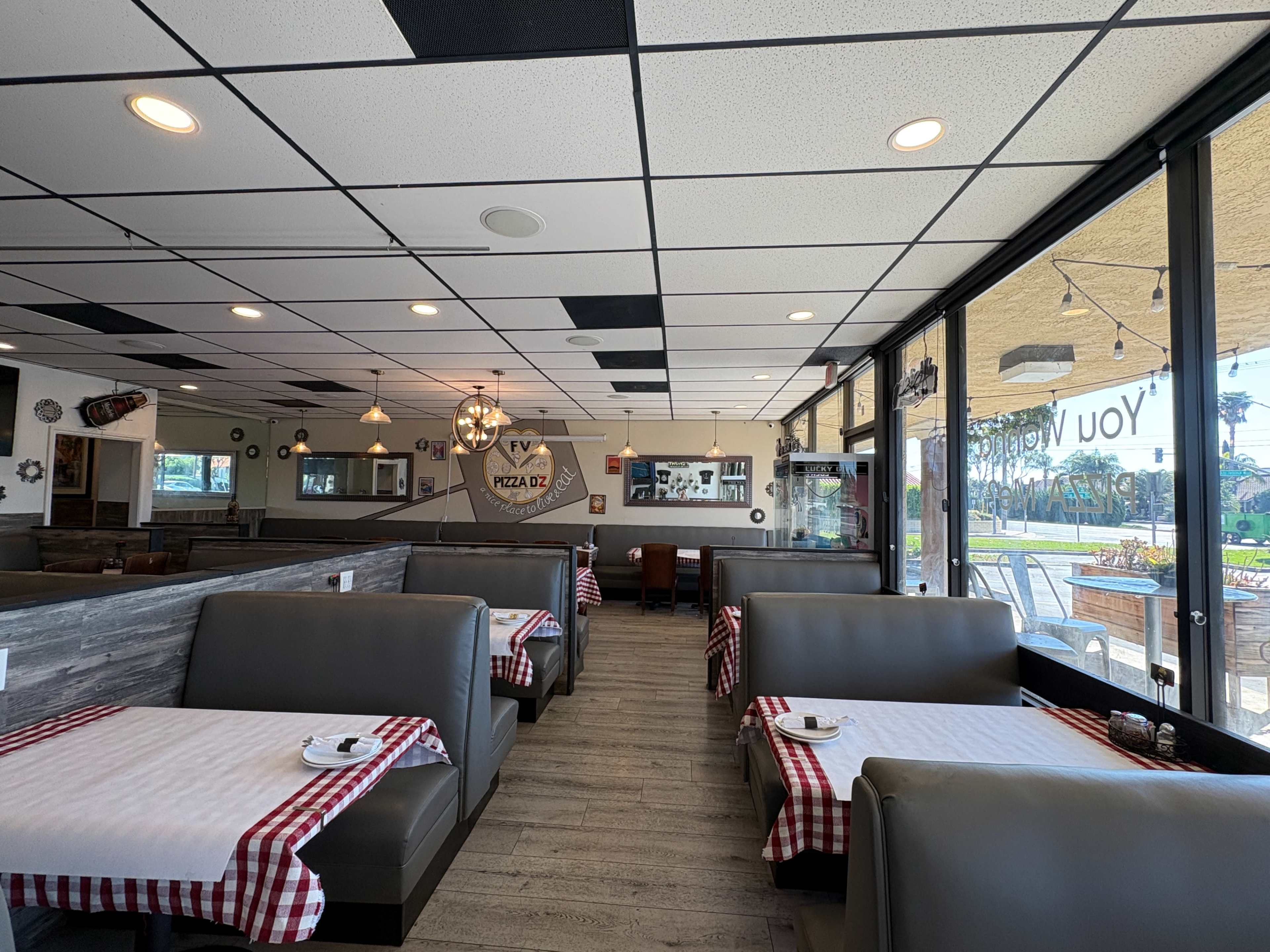 The interior of a restaurant features booth seating with checkered tablecloths and large windows providing natural light.