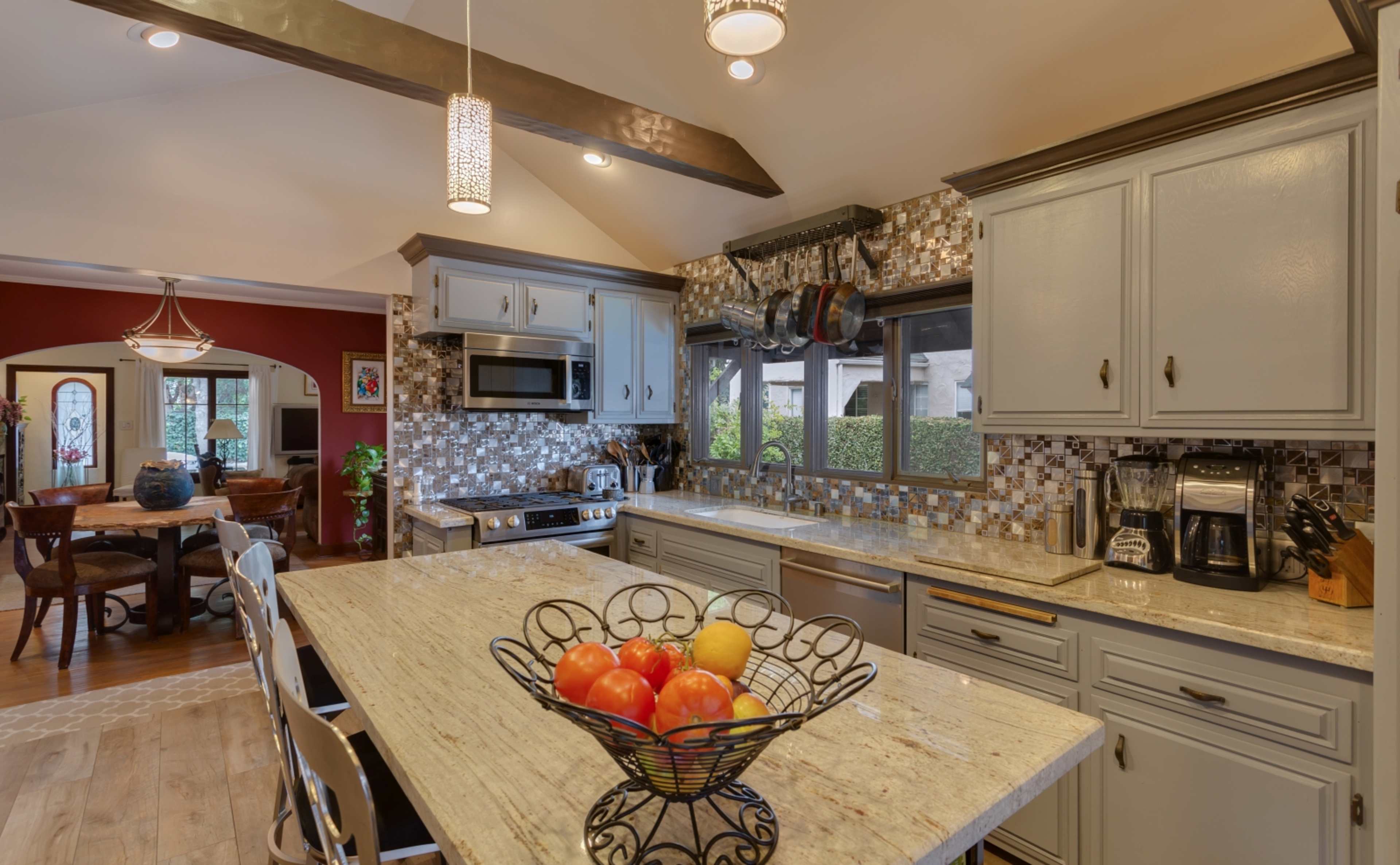 A modern kitchen with a granite island countertop, stainless steel appliances, and a bowl of colorful fruit at the center.