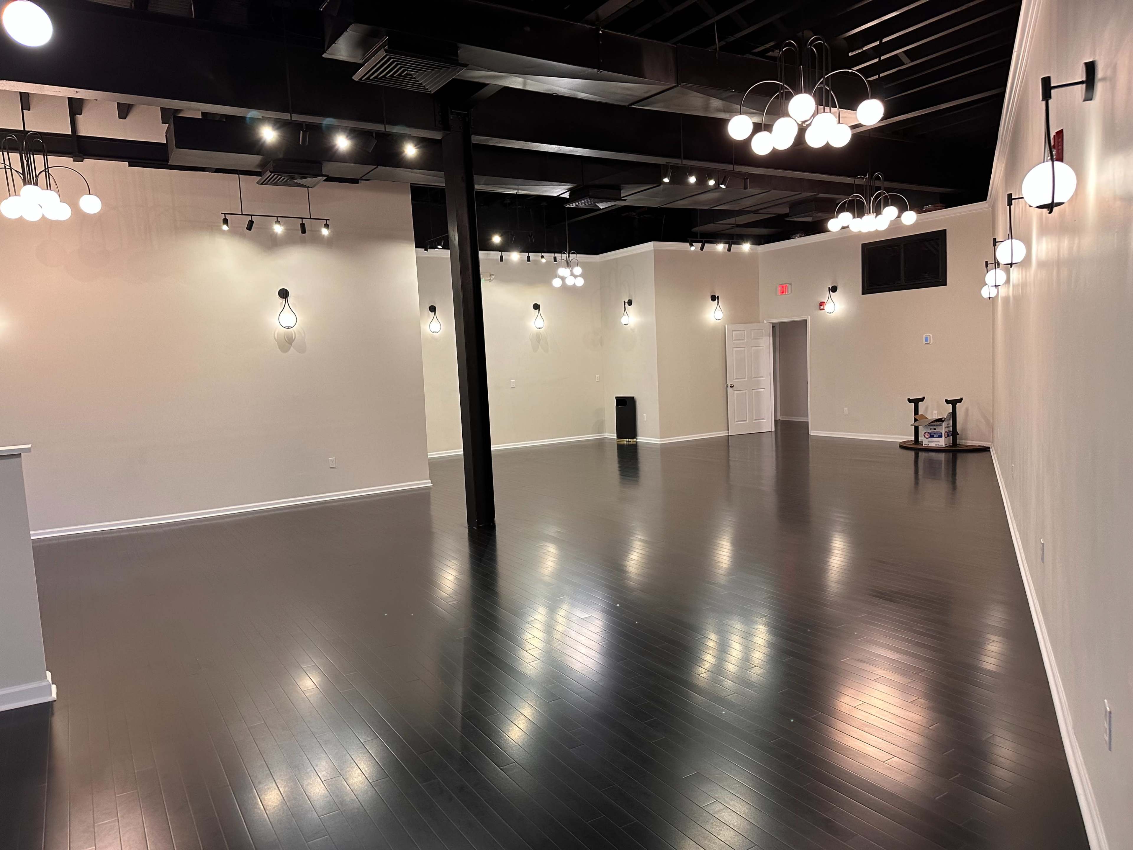 A spacious, empty interior room with dark hardwood floors and several light fixtures hanging from the ceiling.