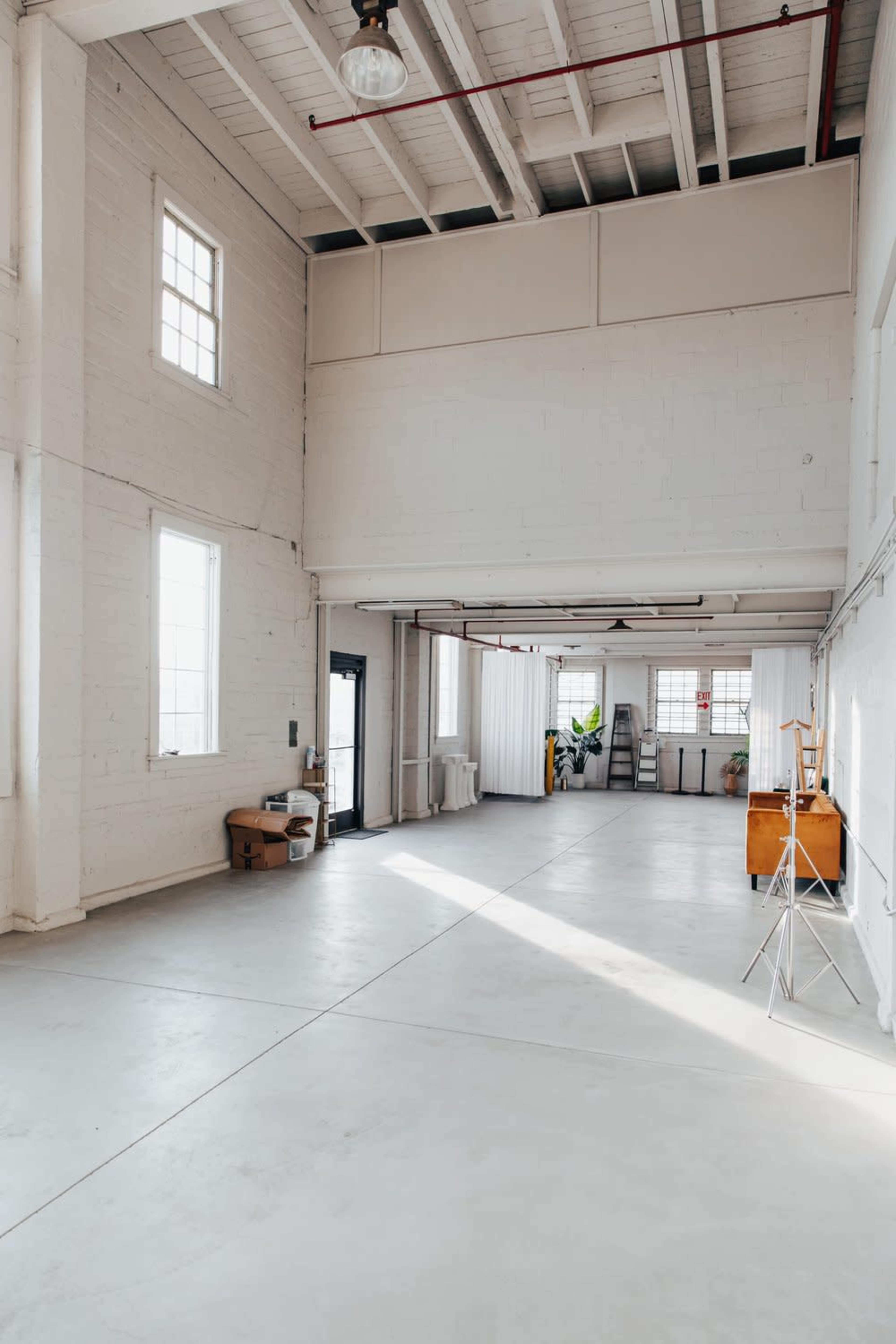 A spacious, empty industrial room with white walls, large windows, and polished concrete flooring.