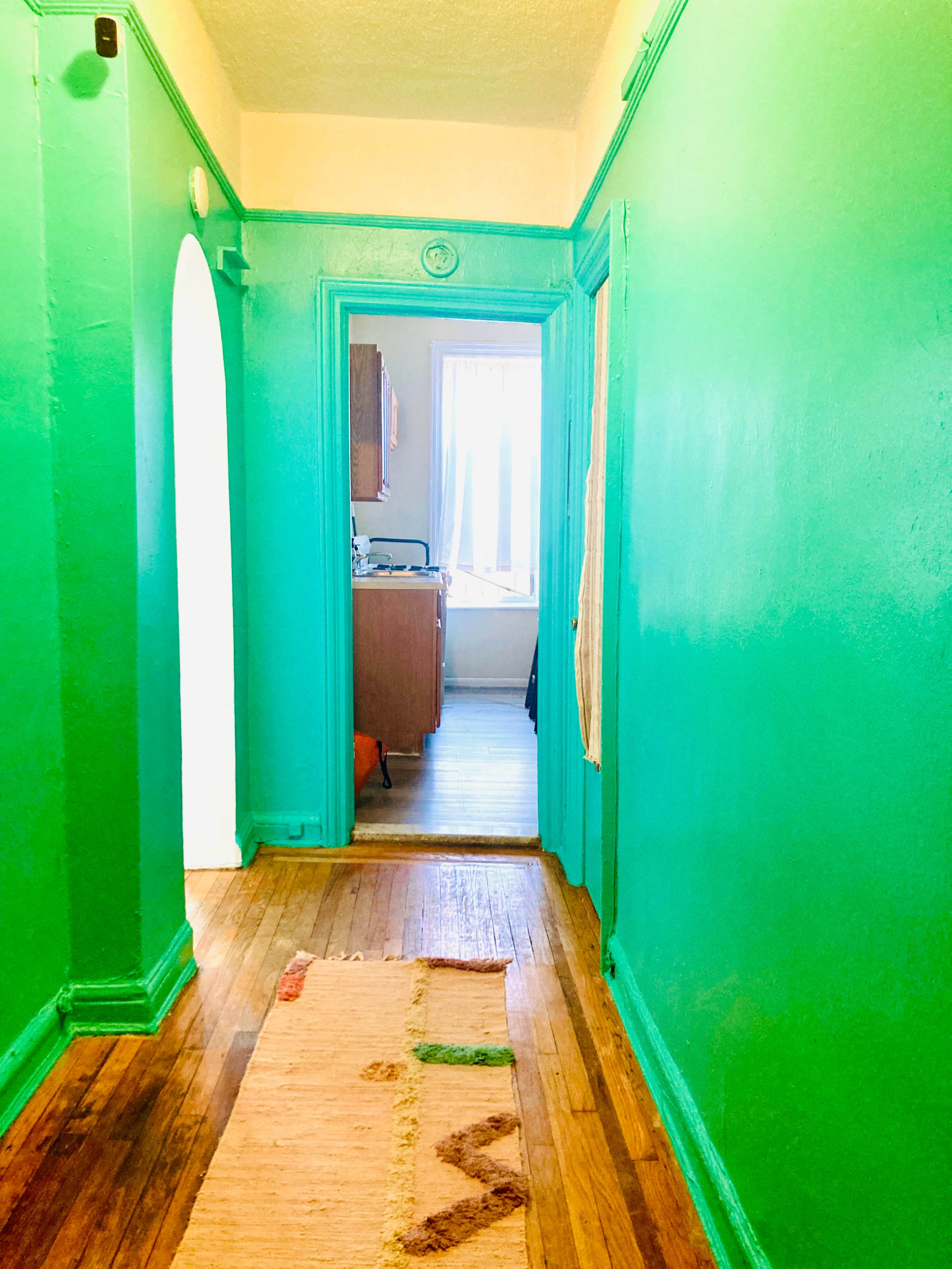 A brightly painted green hallway leads to a kitchen illuminated by natural light.