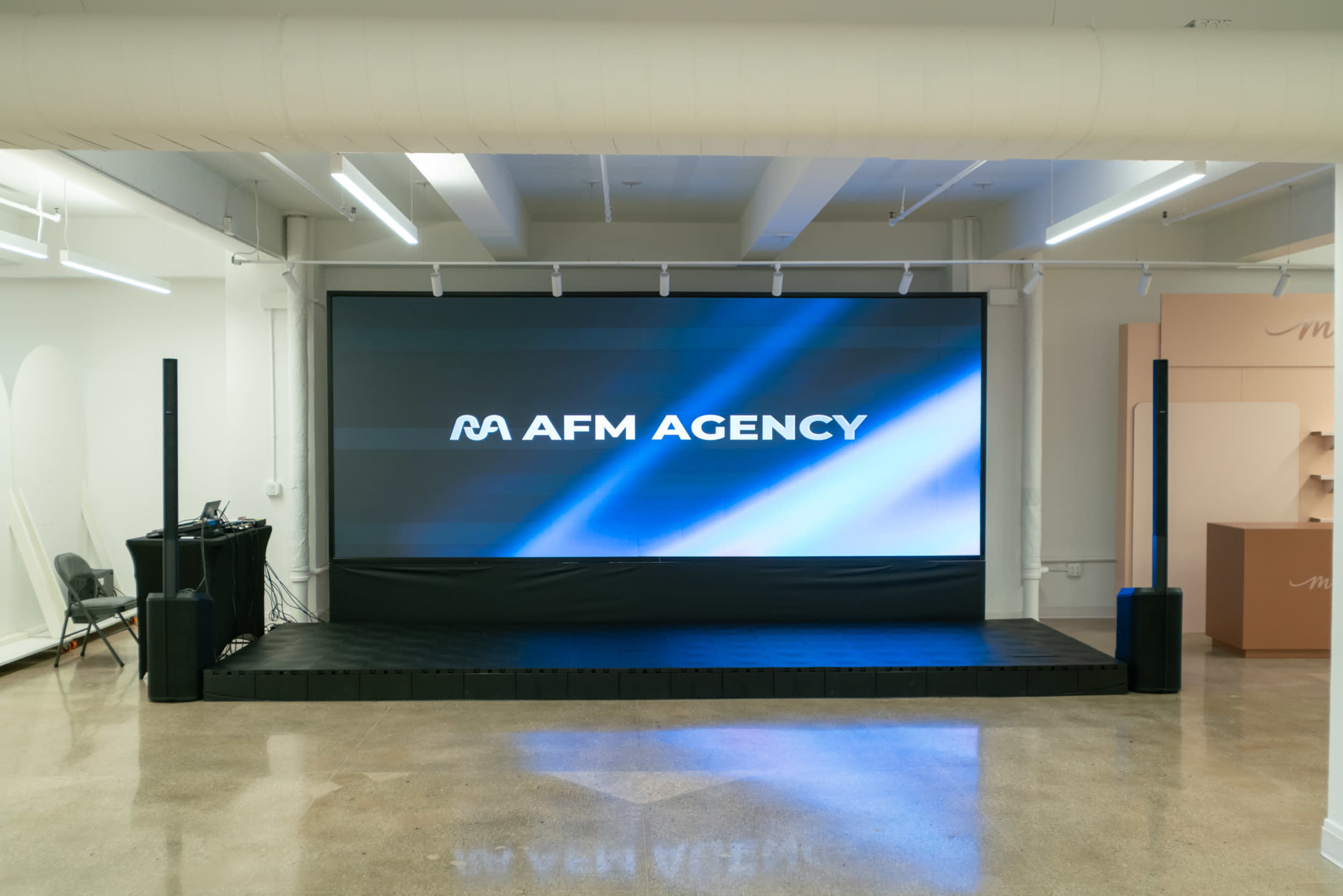 The image shows a modern stage with a large screen displaying the logo of "AFM AGENCY" in a well-lit interior space.