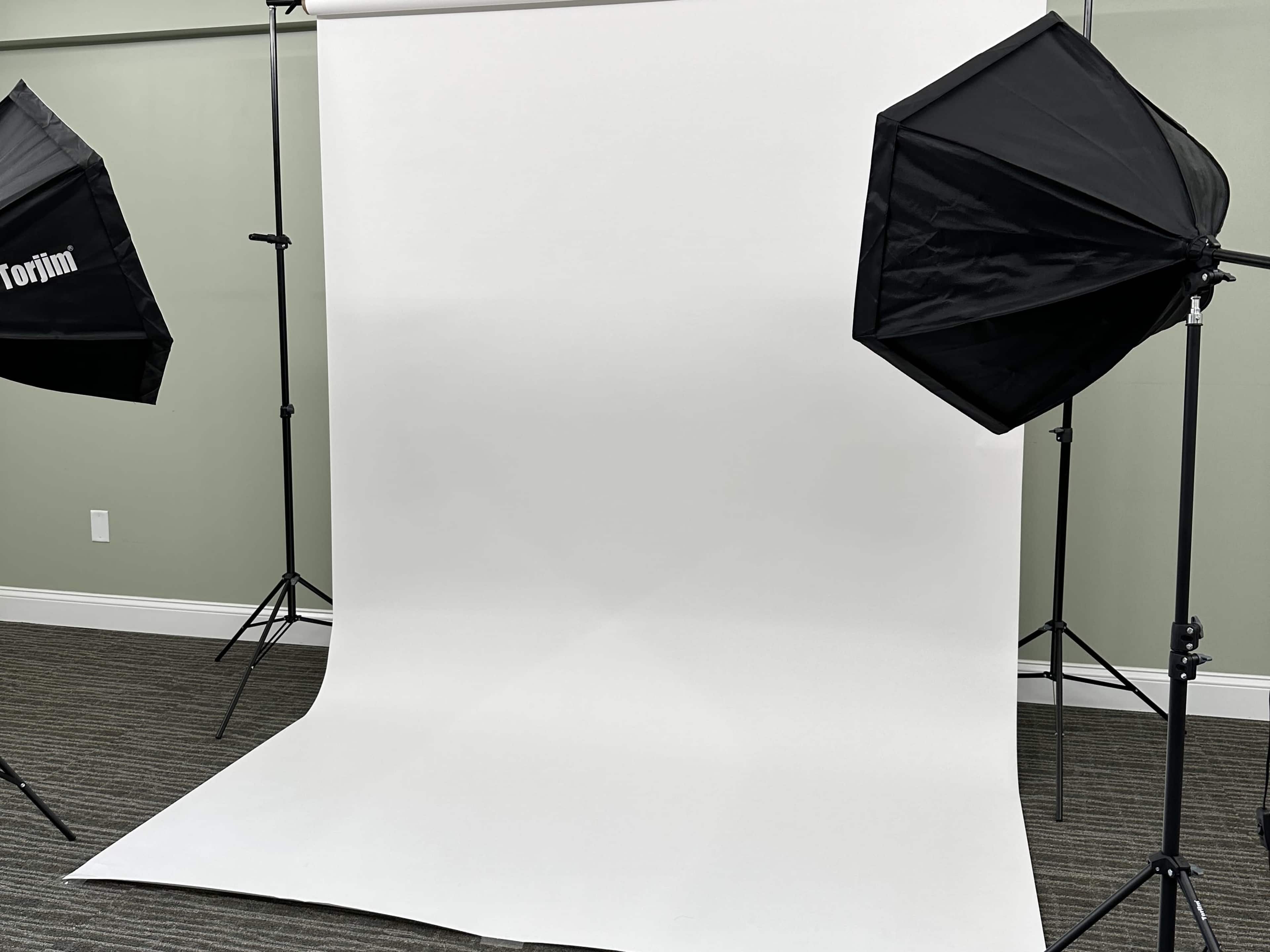 A photography studio setup with a plain white backdrop and two black softboxes positioned on either side.
