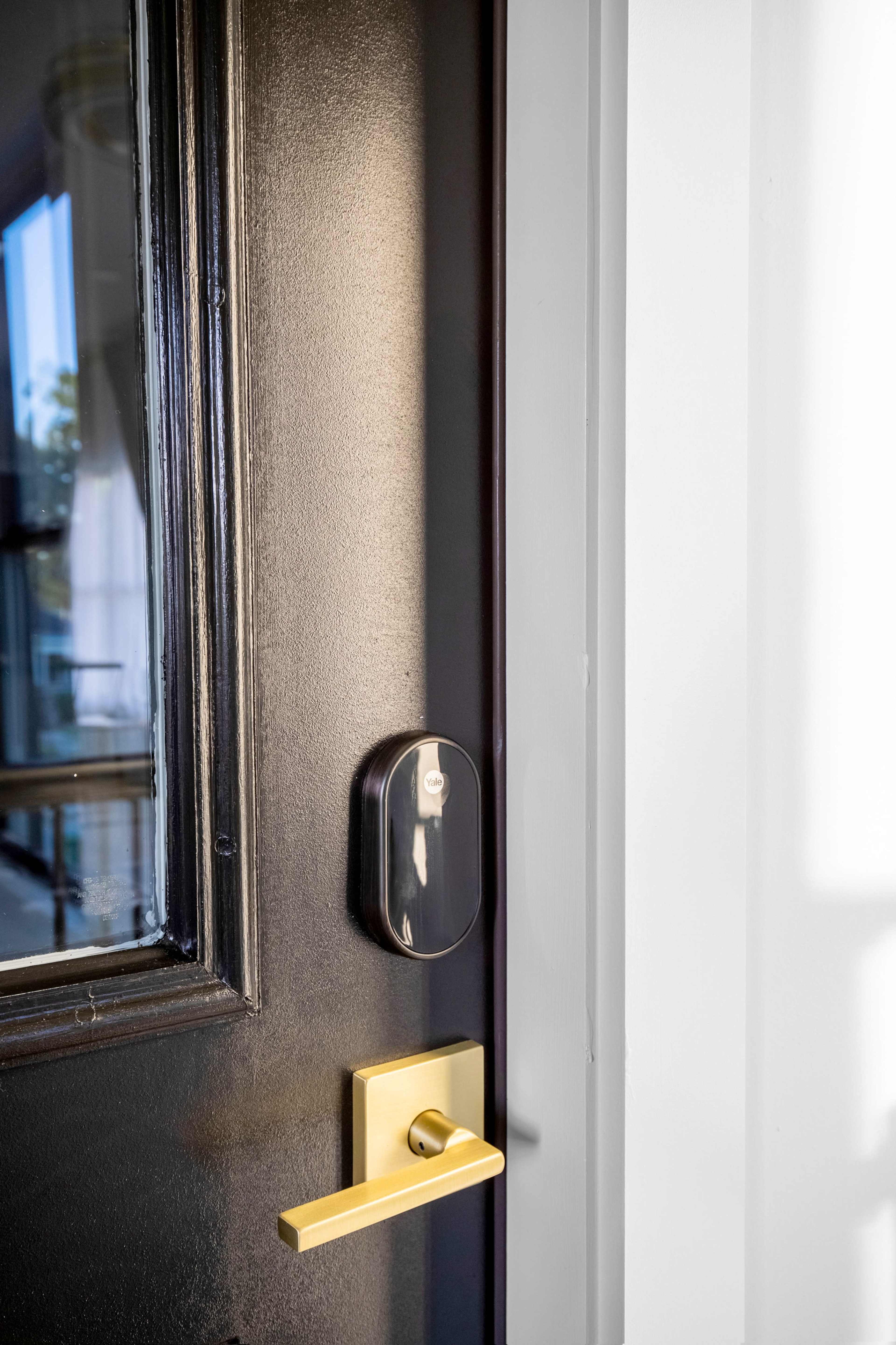 The image shows a black door with a gold handle and a smart lock mounted on the side.