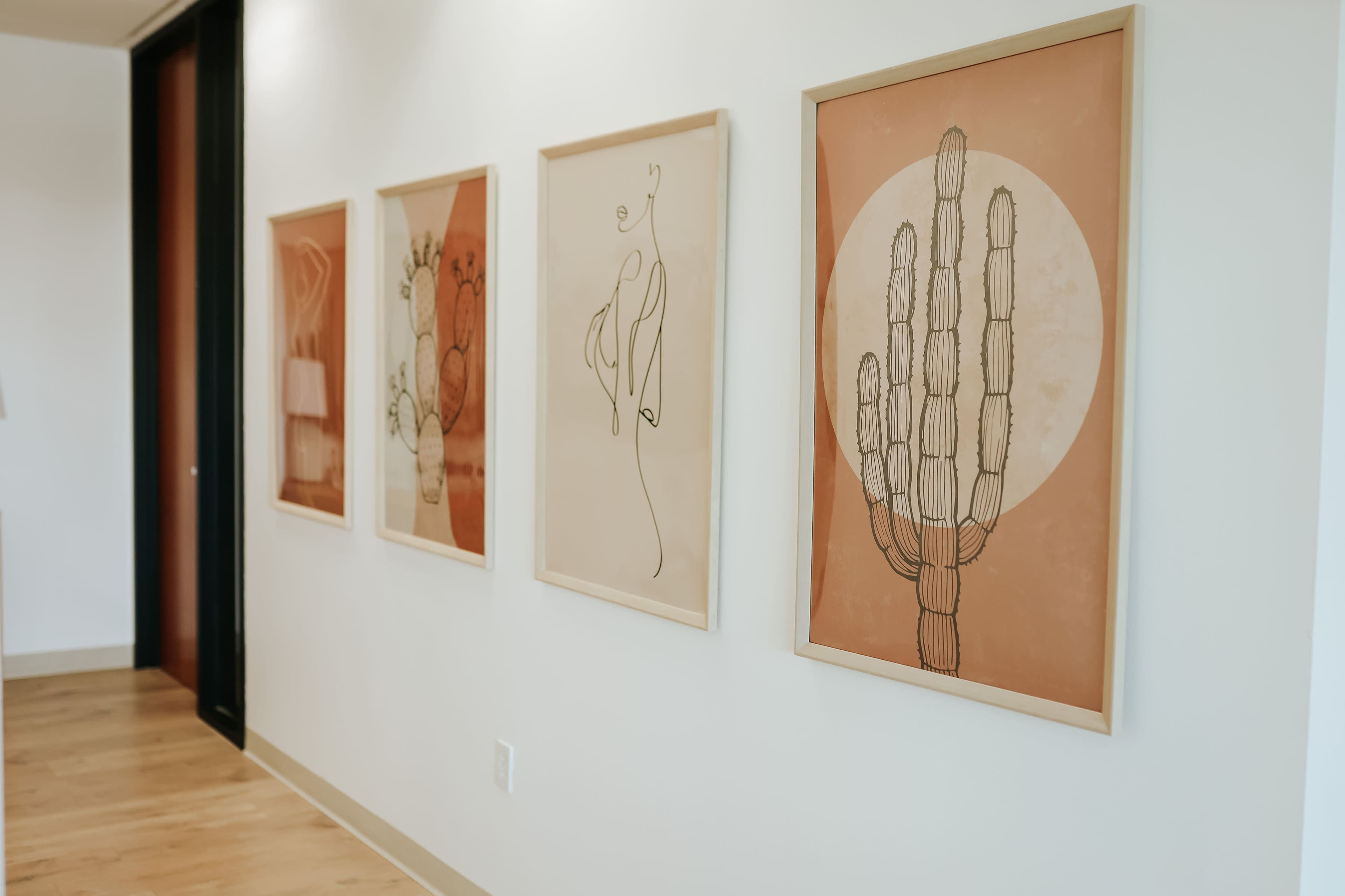 A hallway with four framed art prints featuring line drawings of cacti and abstract figures displayed on a light-colored wall.