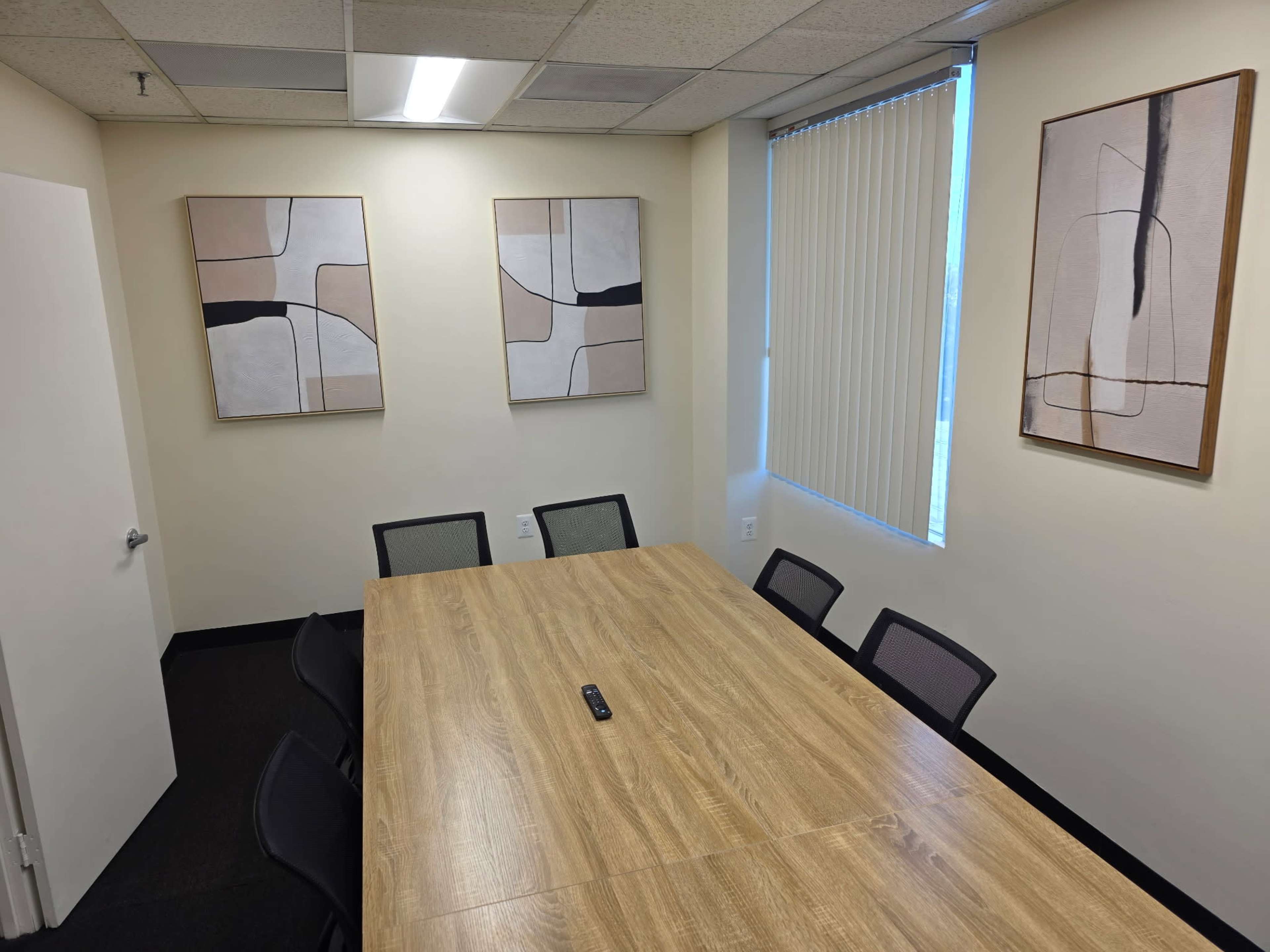 The image shows a conference room with a large wooden table surrounded by chairs, and three abstract art pieces on the walls.