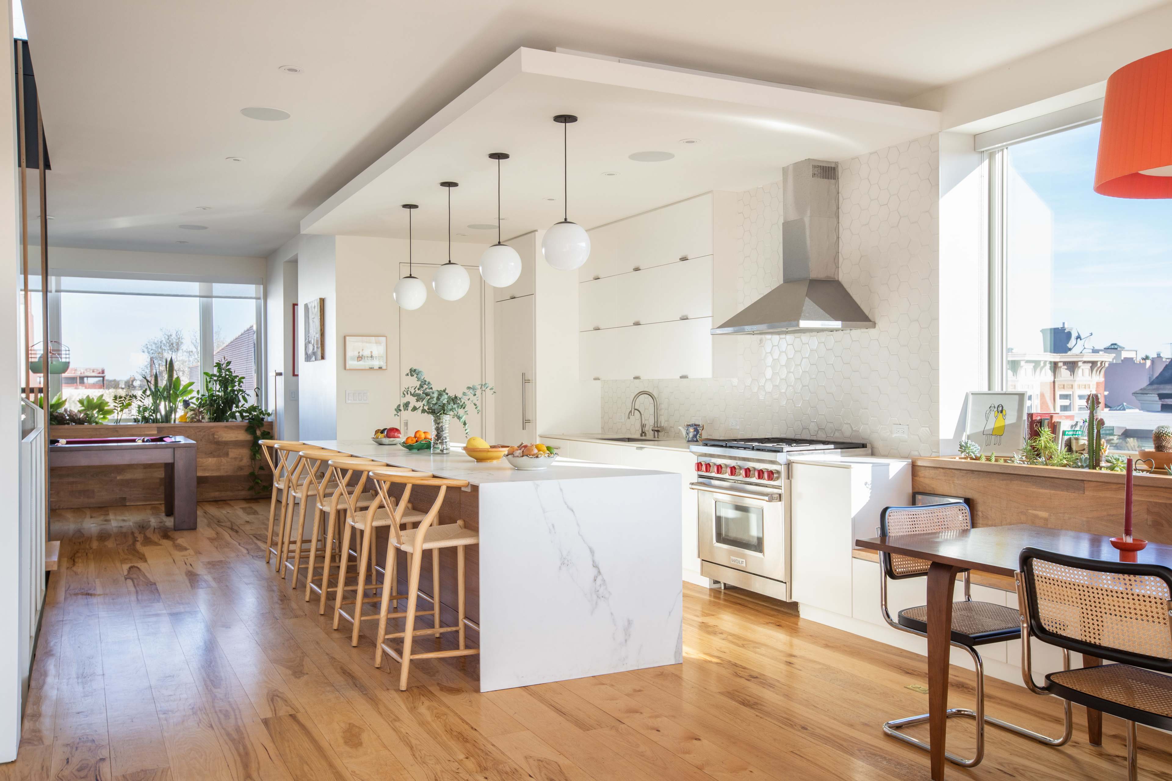 A modern kitchen with a marble island, pendant lights, and wooden flooring, featuring a dining area with a table and chairs.