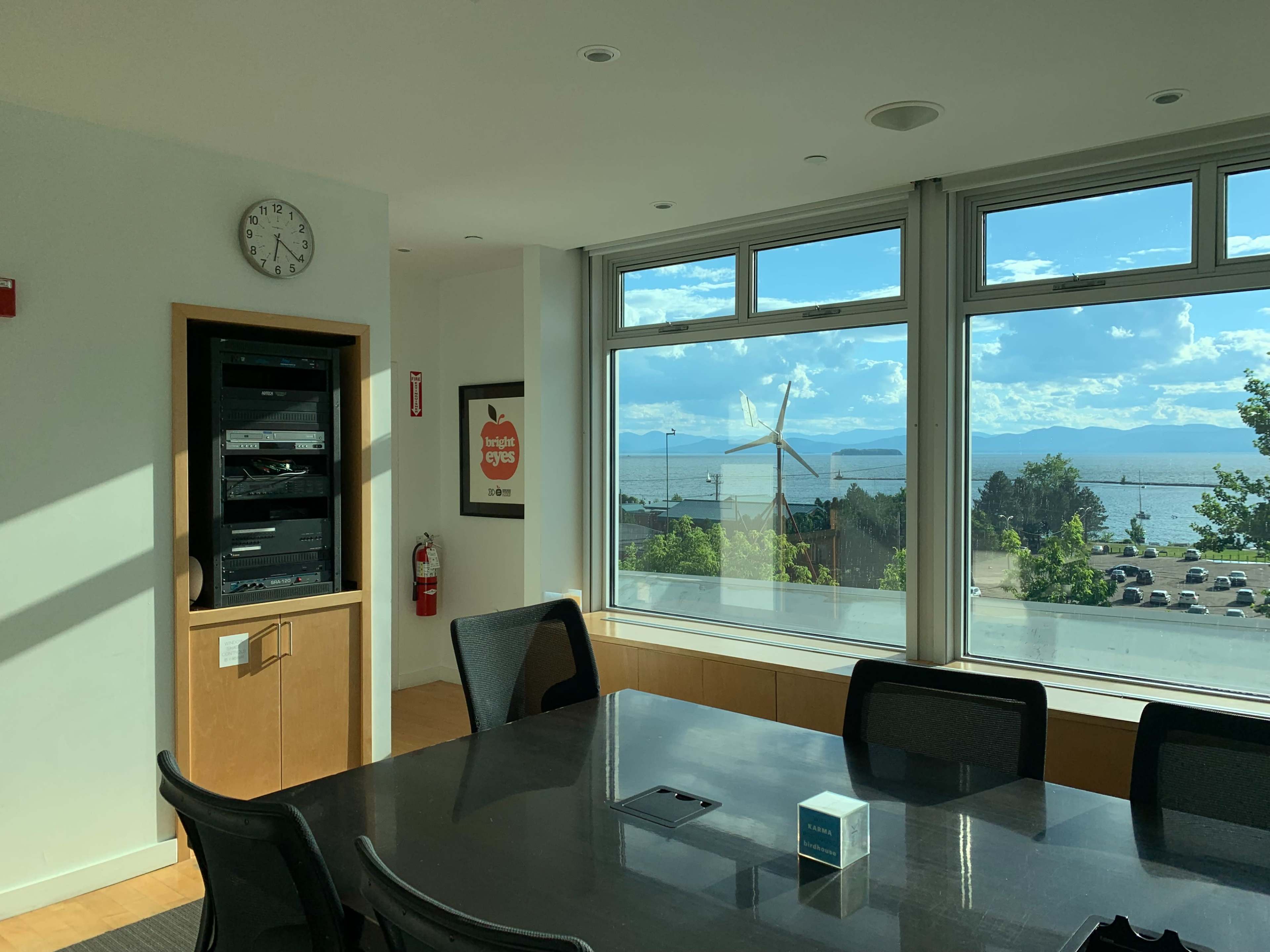 A conference room features a large table and a view of a body of water and a wind turbine through windows.