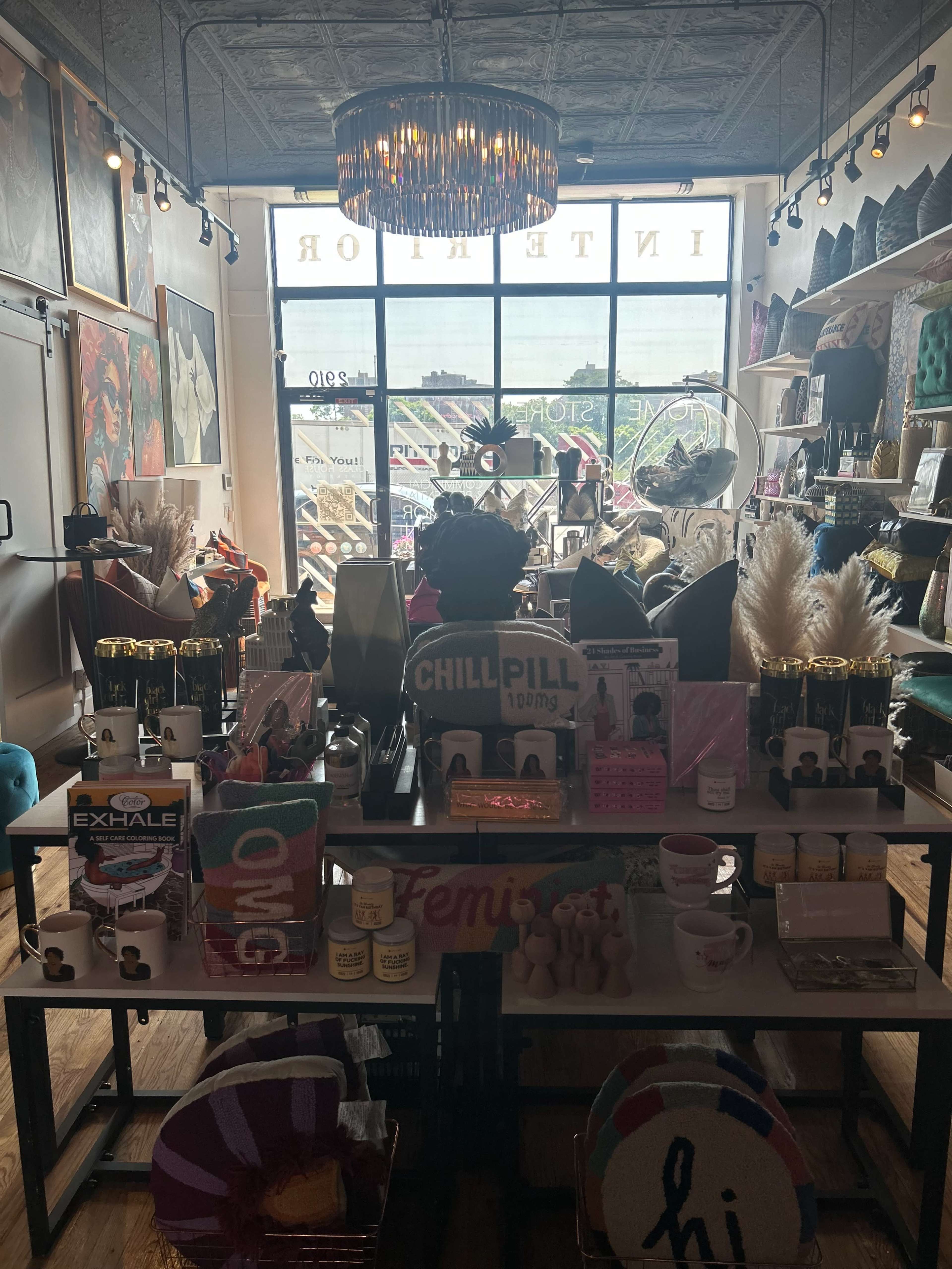 A boutique interior with shelves displaying various decorative items, candles, and gifts, under a large, ornate light fixture.