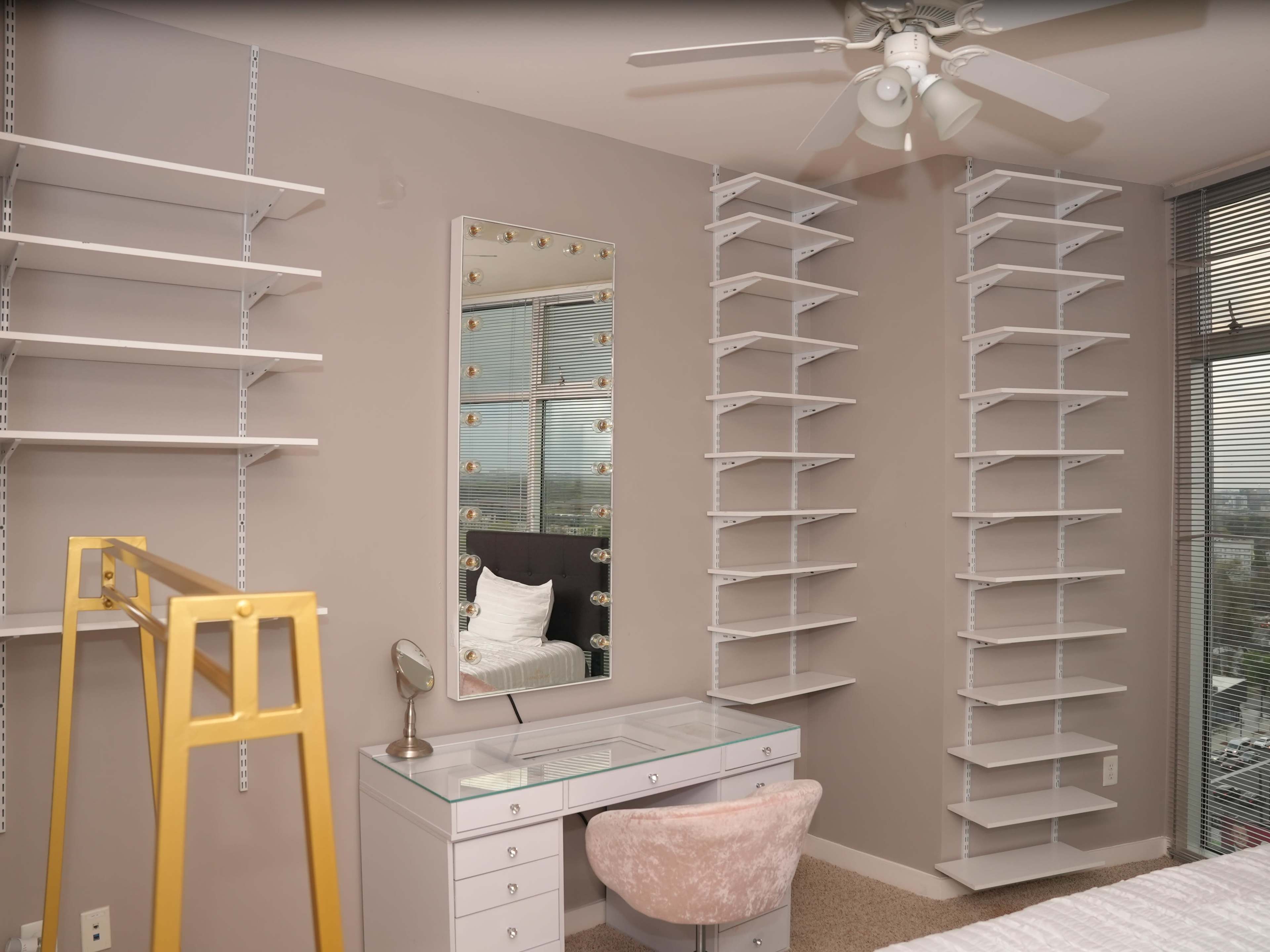 A modern bedroom with a wall-mounted mirror, a white desk with a chair, and multiple wall shelves arranged symmetrically on either side.