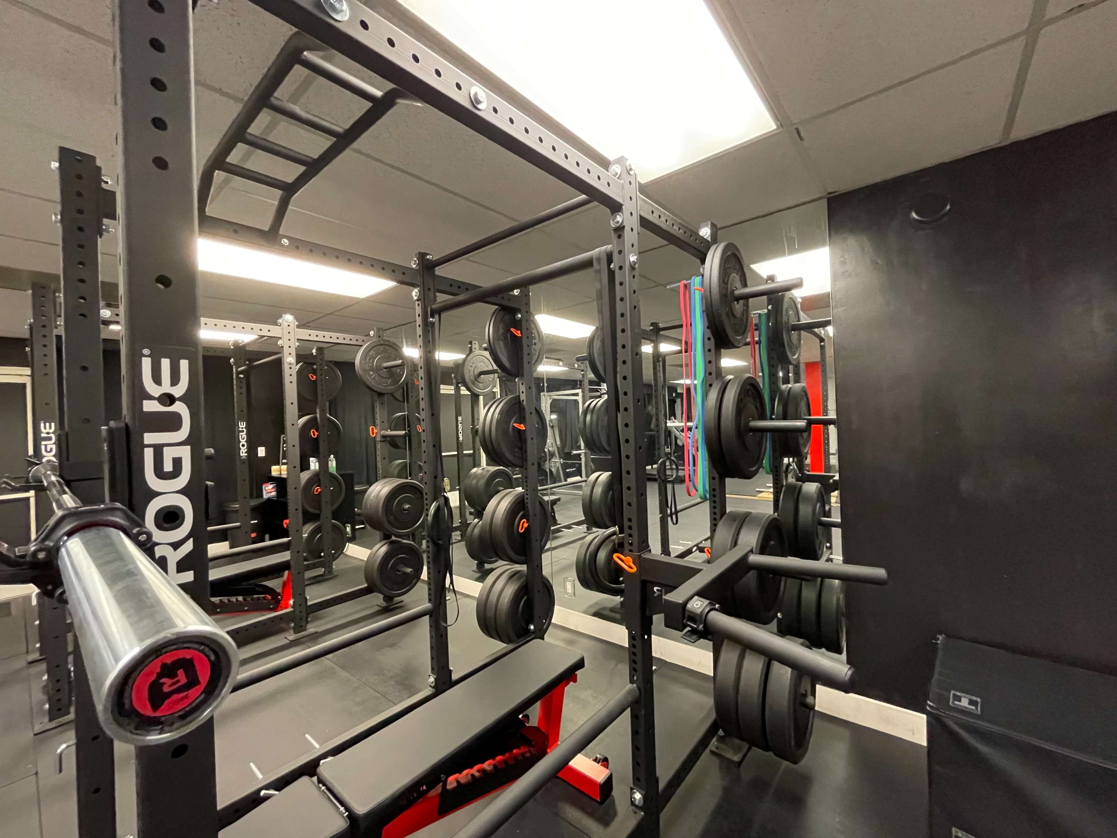 A gym area with a weight rack filled with plates, a squat rack, and a bench, all set against a black wall.